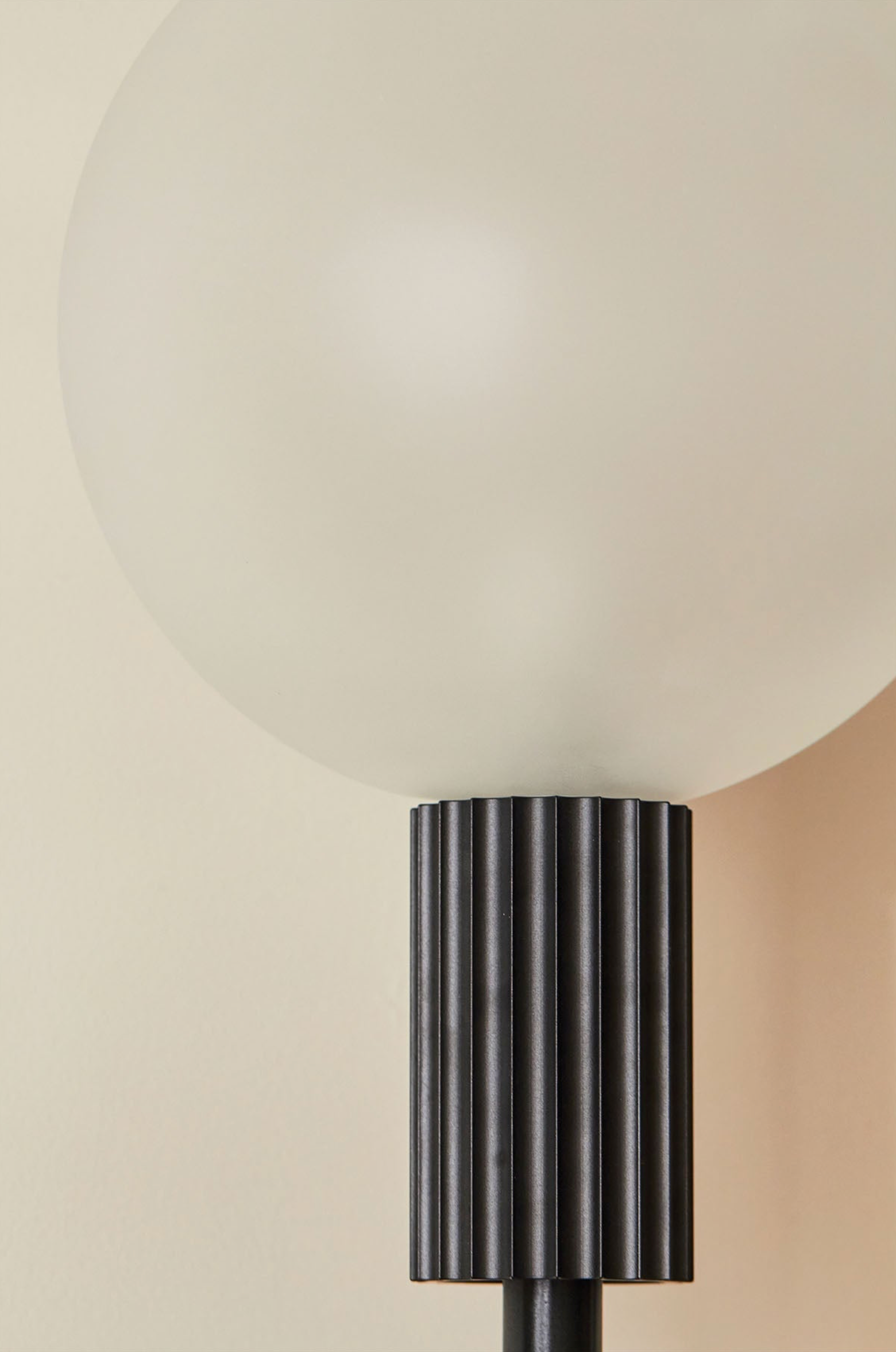 Close-up of an indoor wall lamp with a ribbed black base and white shade on a beige background