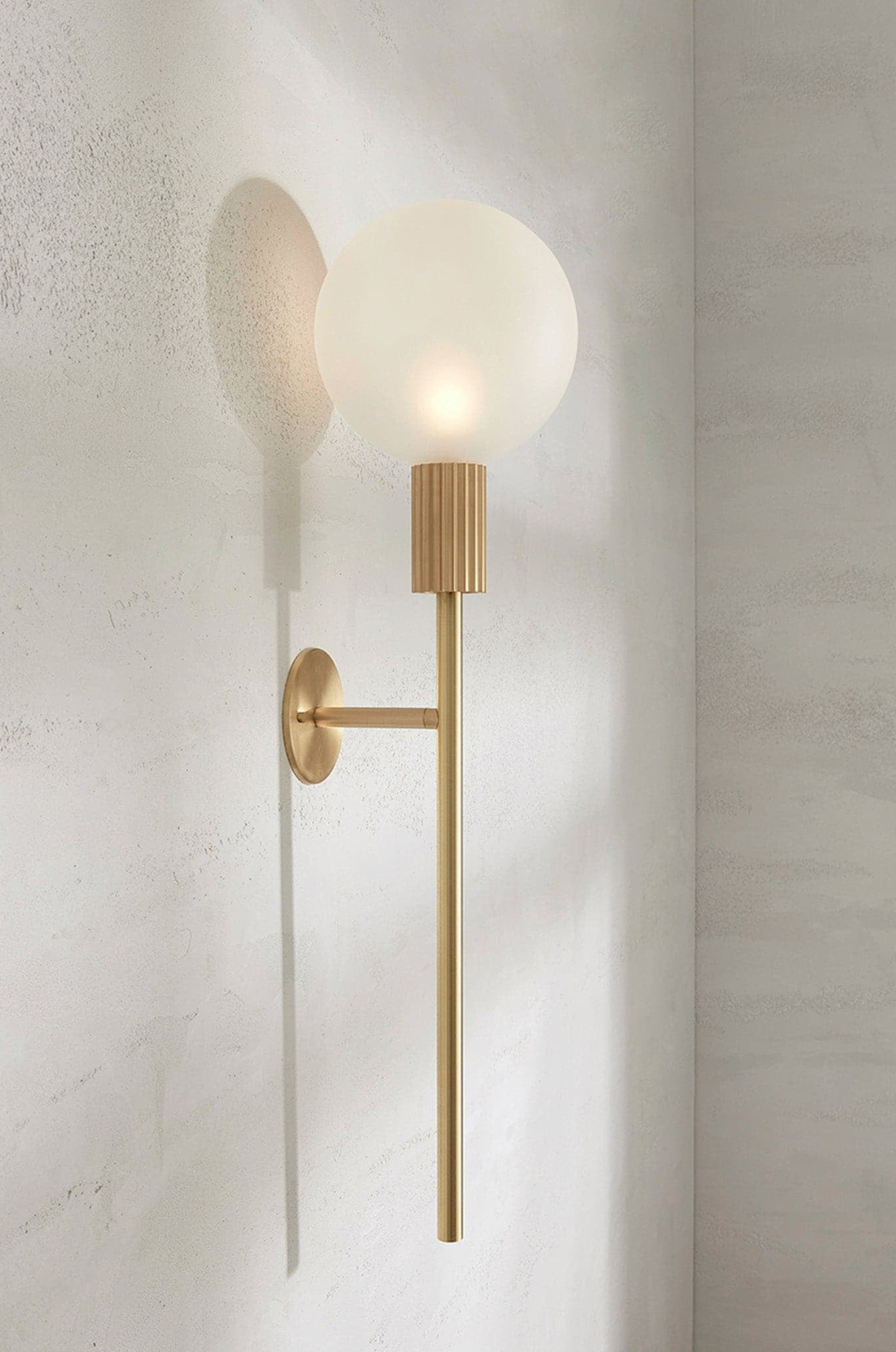 Modern wall sconce with a gold finish and white glass shade on a neutral wall.