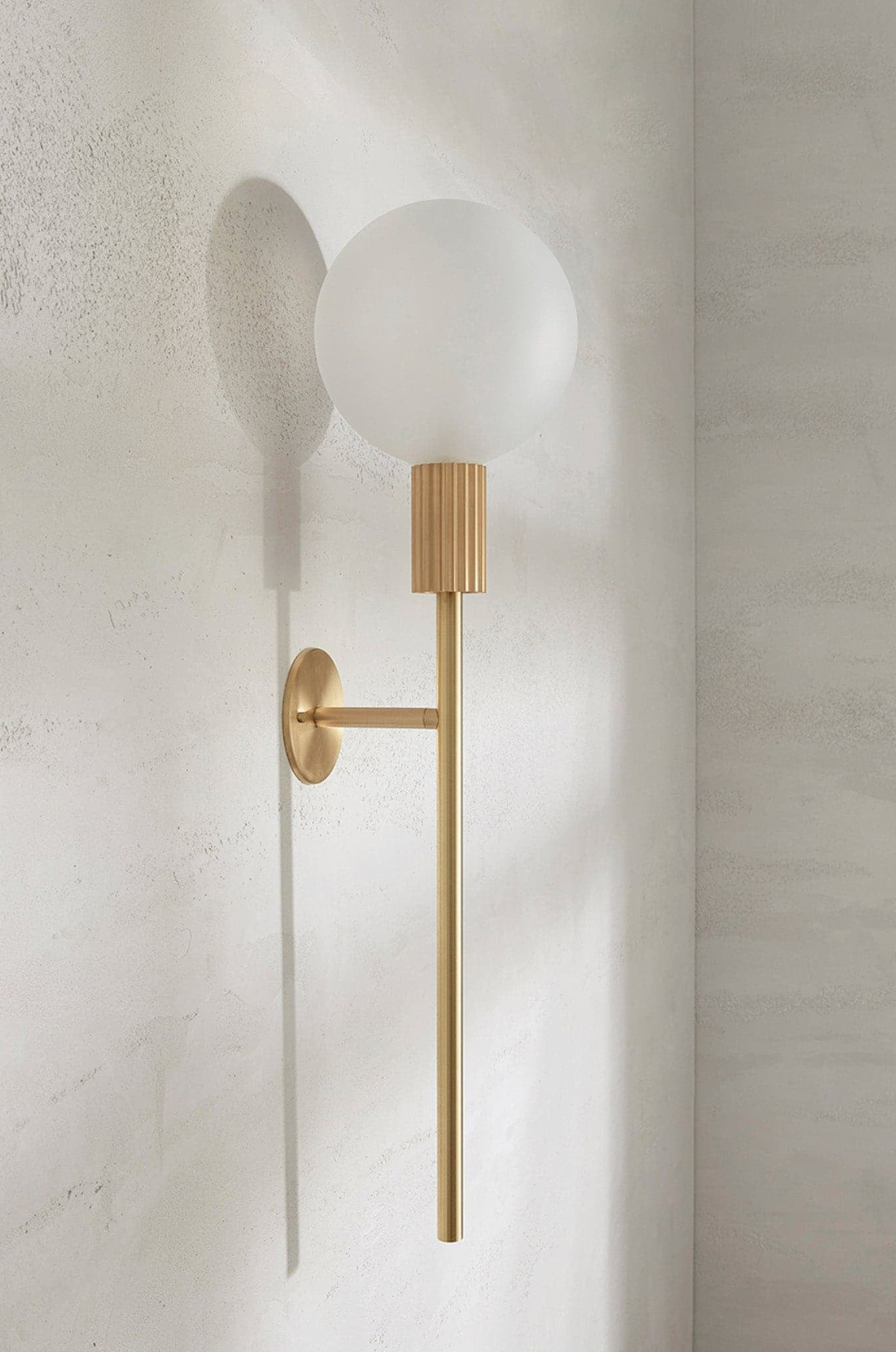 Wall-mounted light fixture with a gold finish and frosted glass shade on a textured wall.