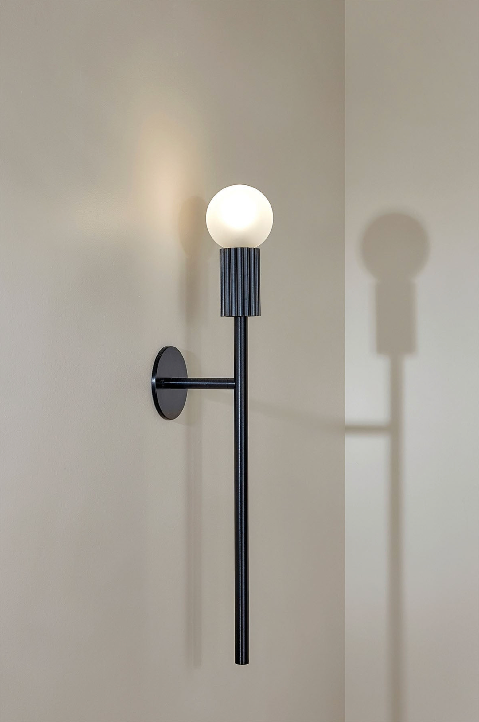 Modern wall-mounted indoor light fixture with a spherical bulb on a neutral background