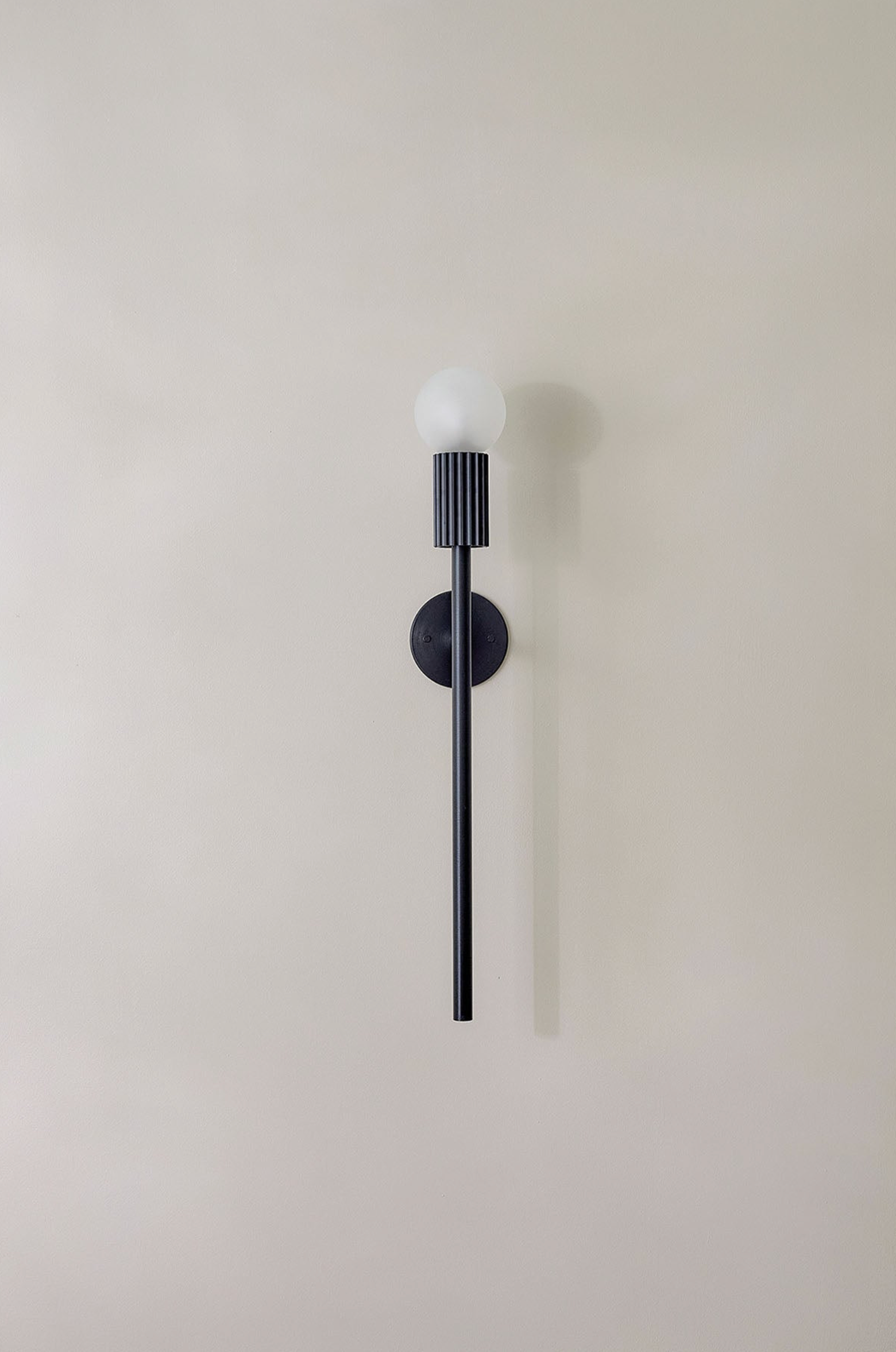 Wall-mounted indoor light fixture with black cylindrical design on a plain wall.