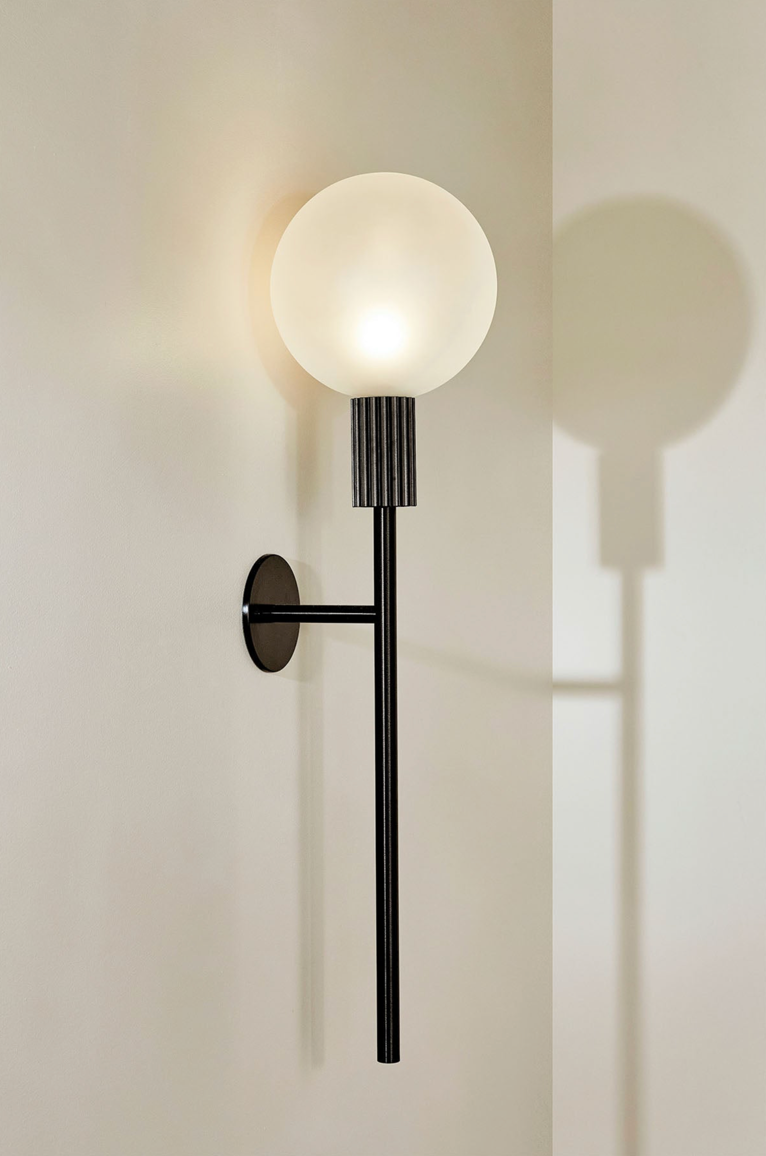 Wall-mounted lamp with a round glass shade on a light beige wall.