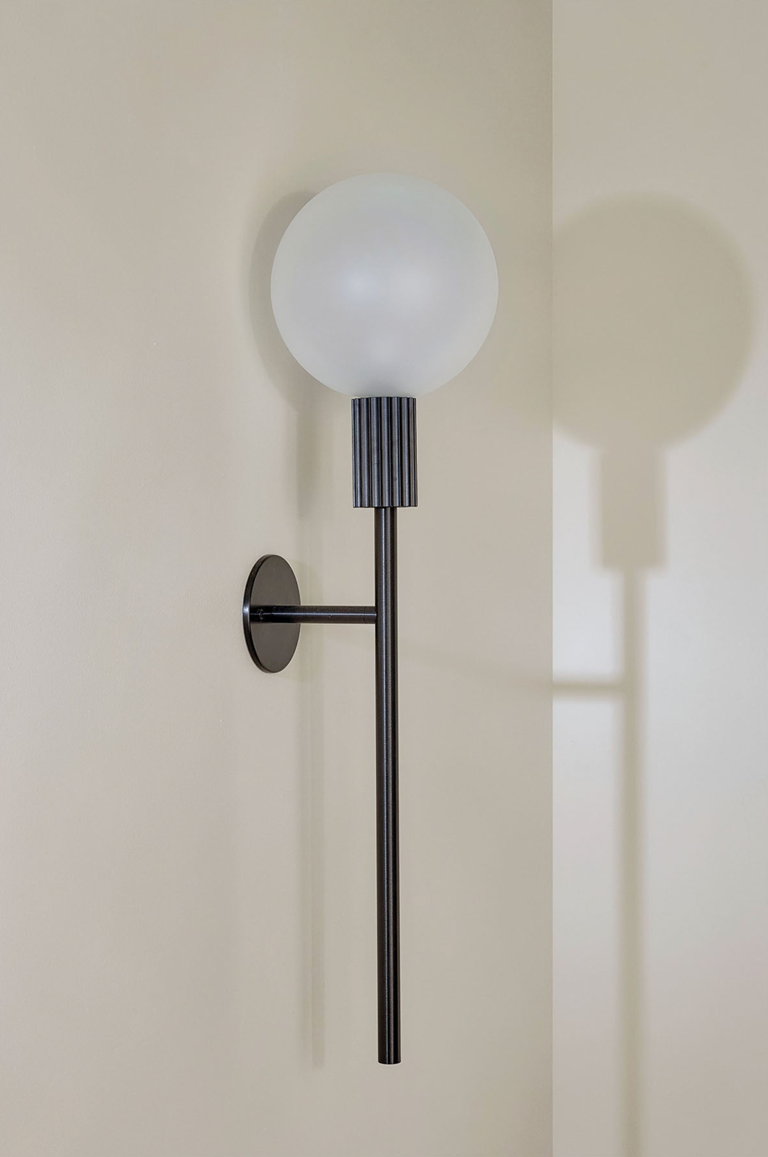 Modern wall lamp with a black fixture and white glass shade on a neutral wall.