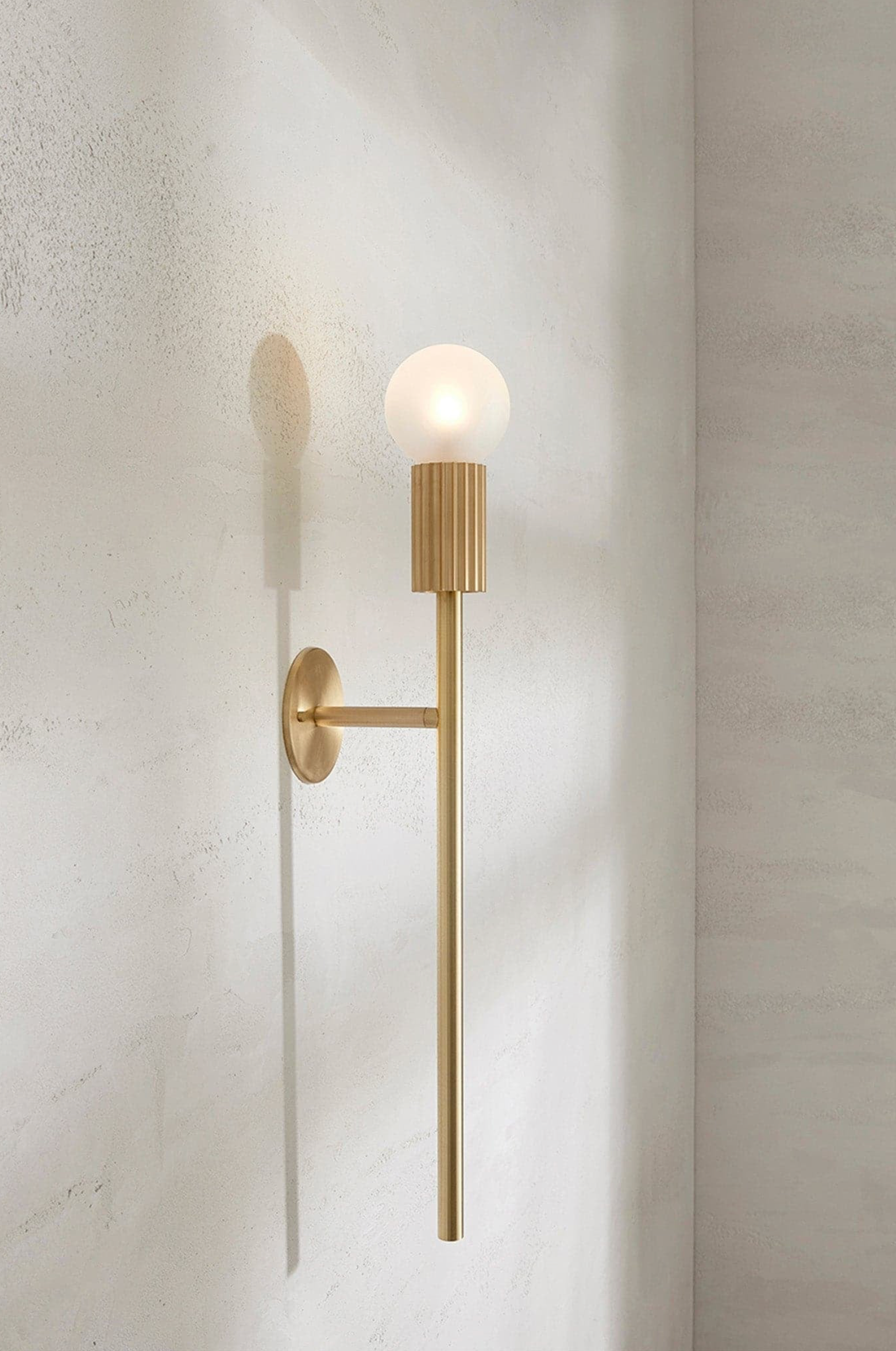 Gold wall sconce with a single bulb on a textured wall
