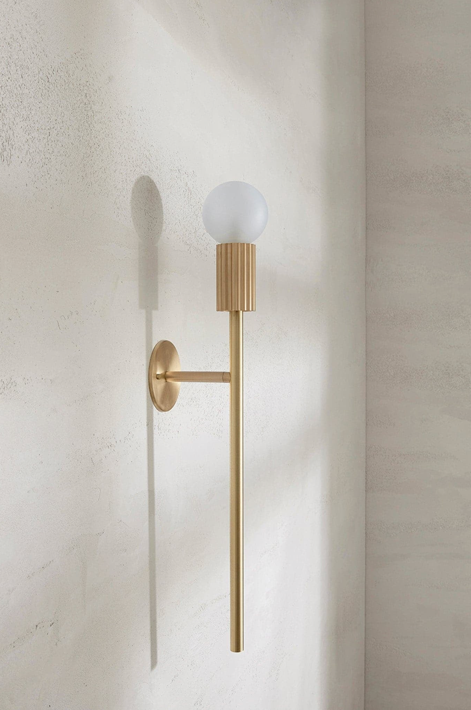 Brass wall sconce with a white bulb on a textured wall