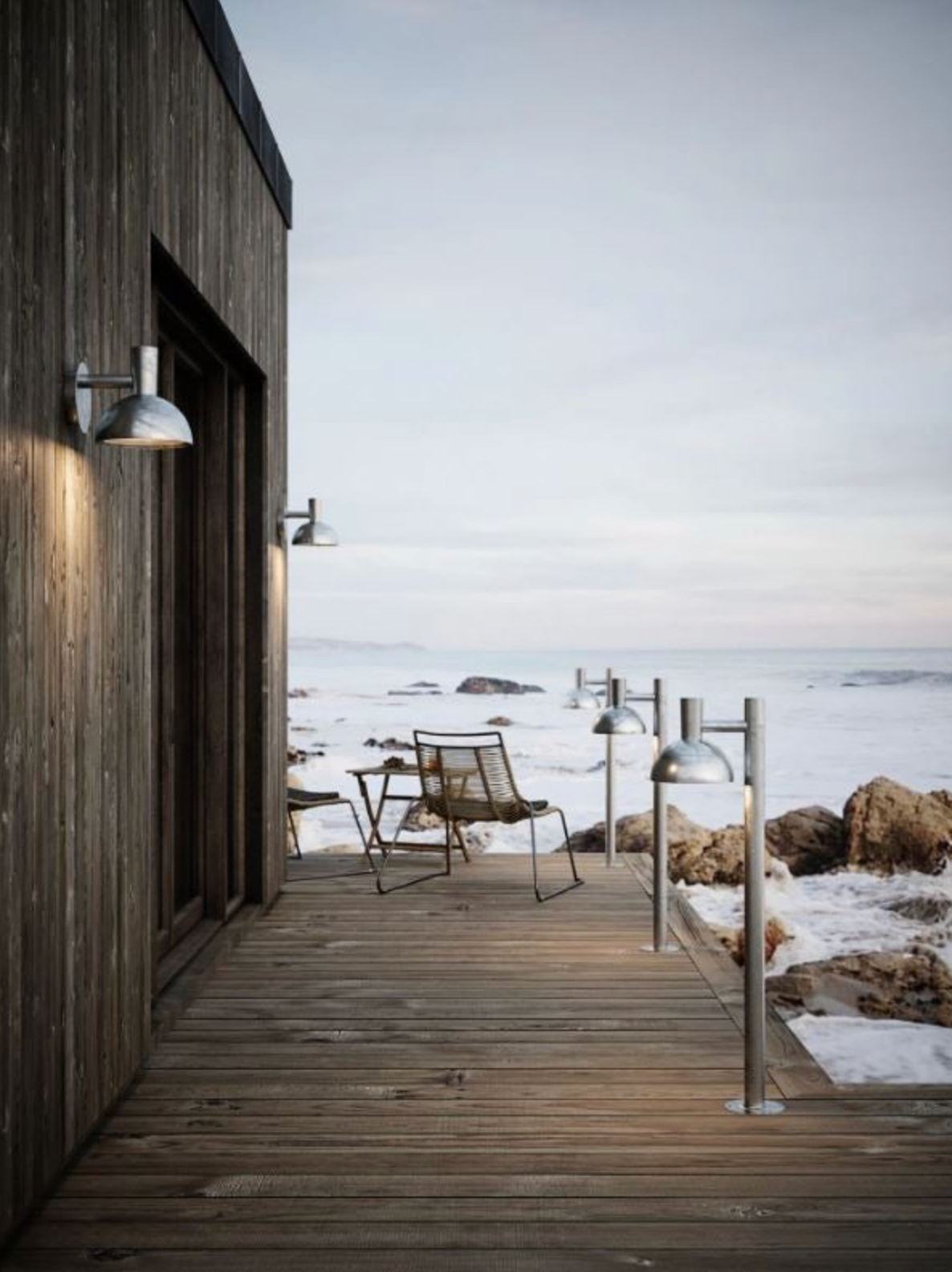 Wooden cabin with outdoor wall lights  a deck overlooking a snowy landscape