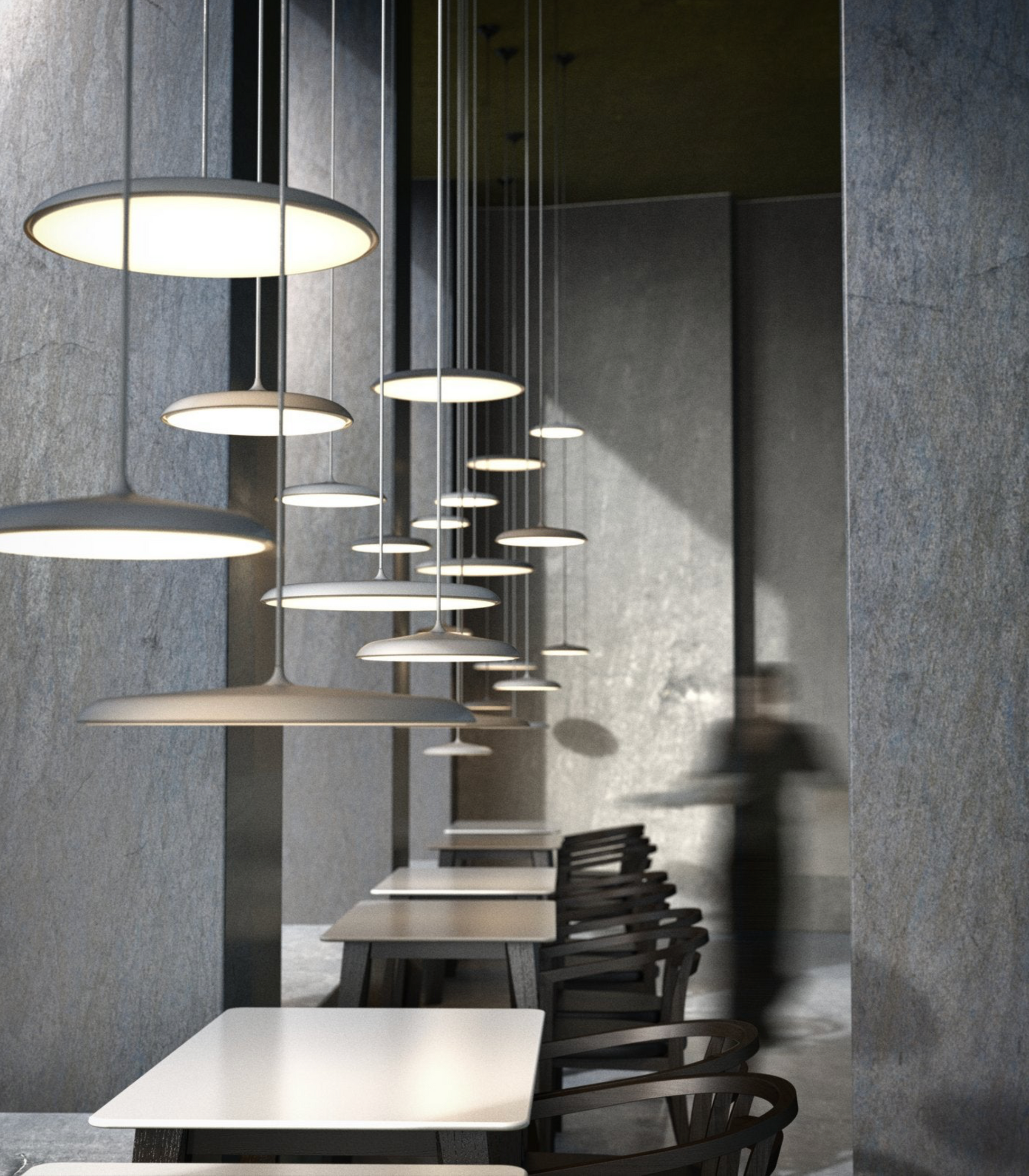 Modern pendant lights hanging in a restaurant dining area with tables and chairs.
