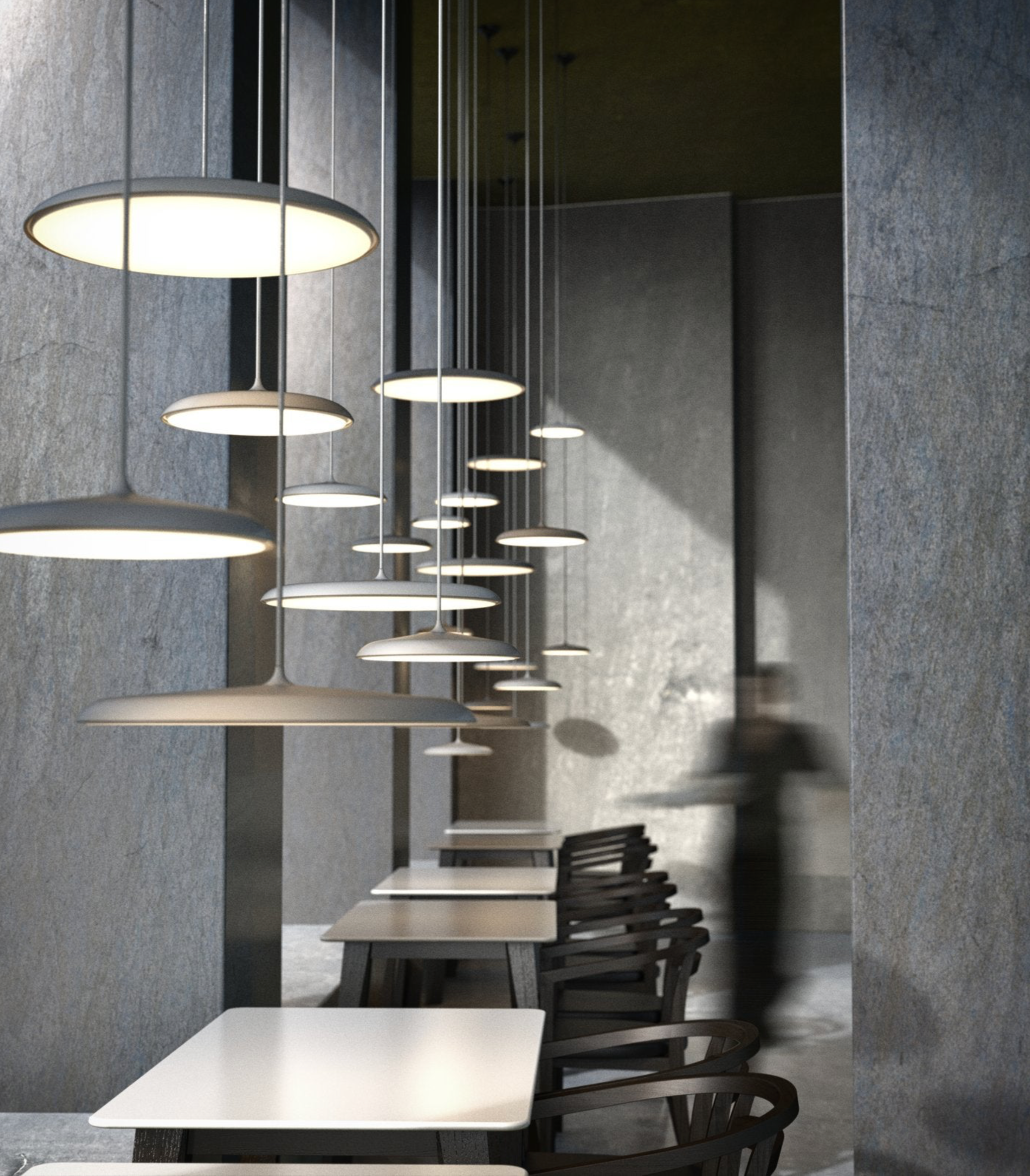 Modern pendant lights hanging in a restaurant dining area with tables and chairs.