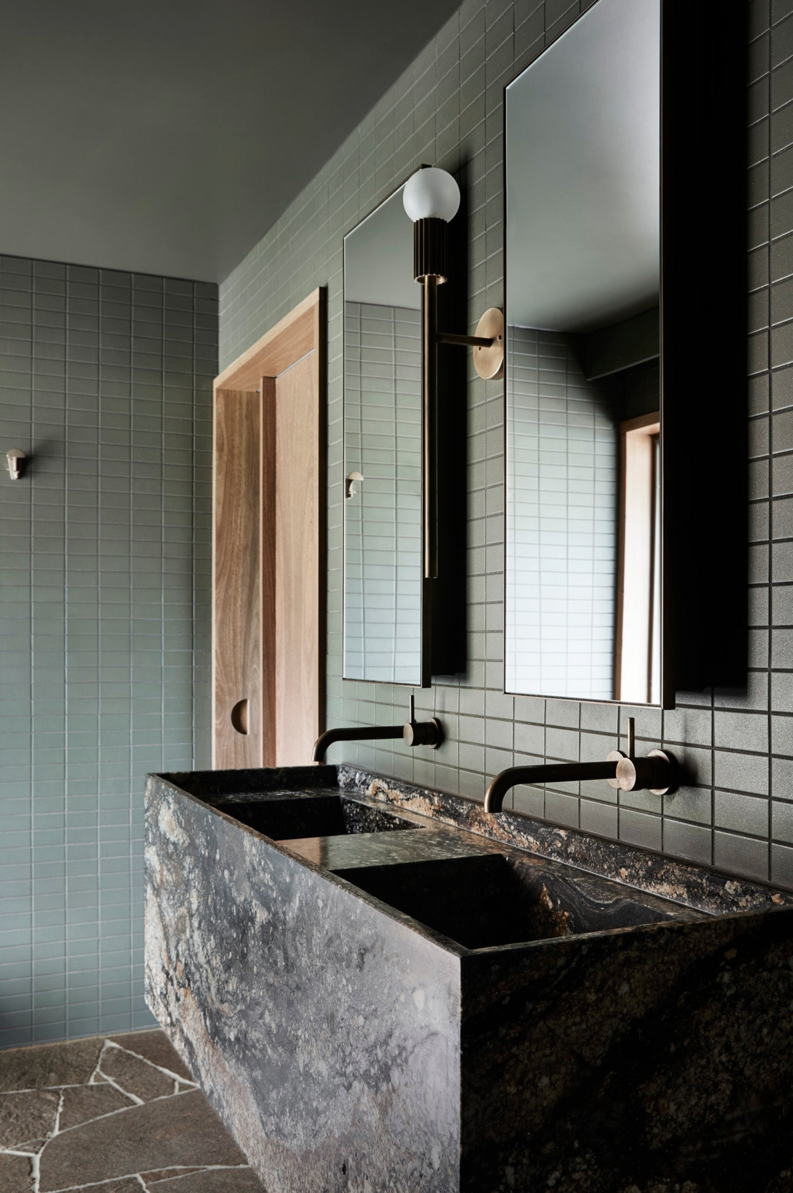 Modern bathroom with black wall light, dark stone vanity and tiled walls.