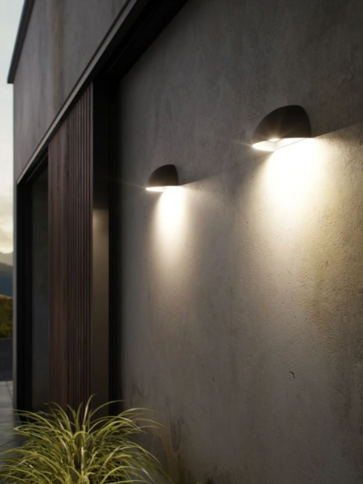 Two outdoor wall lights on a building exterior with a plant in the foreground.
