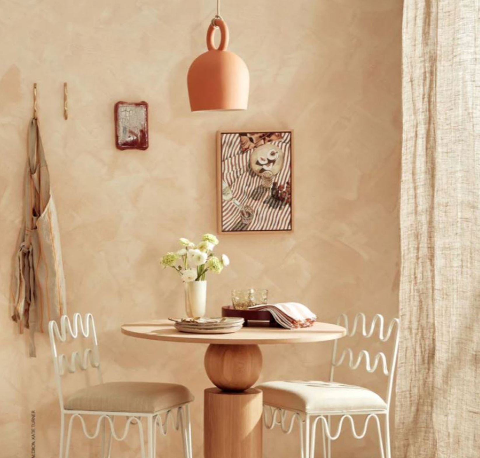 Small dining area with a round table, terracotta clay pendant light and two chairs against a beige wall.