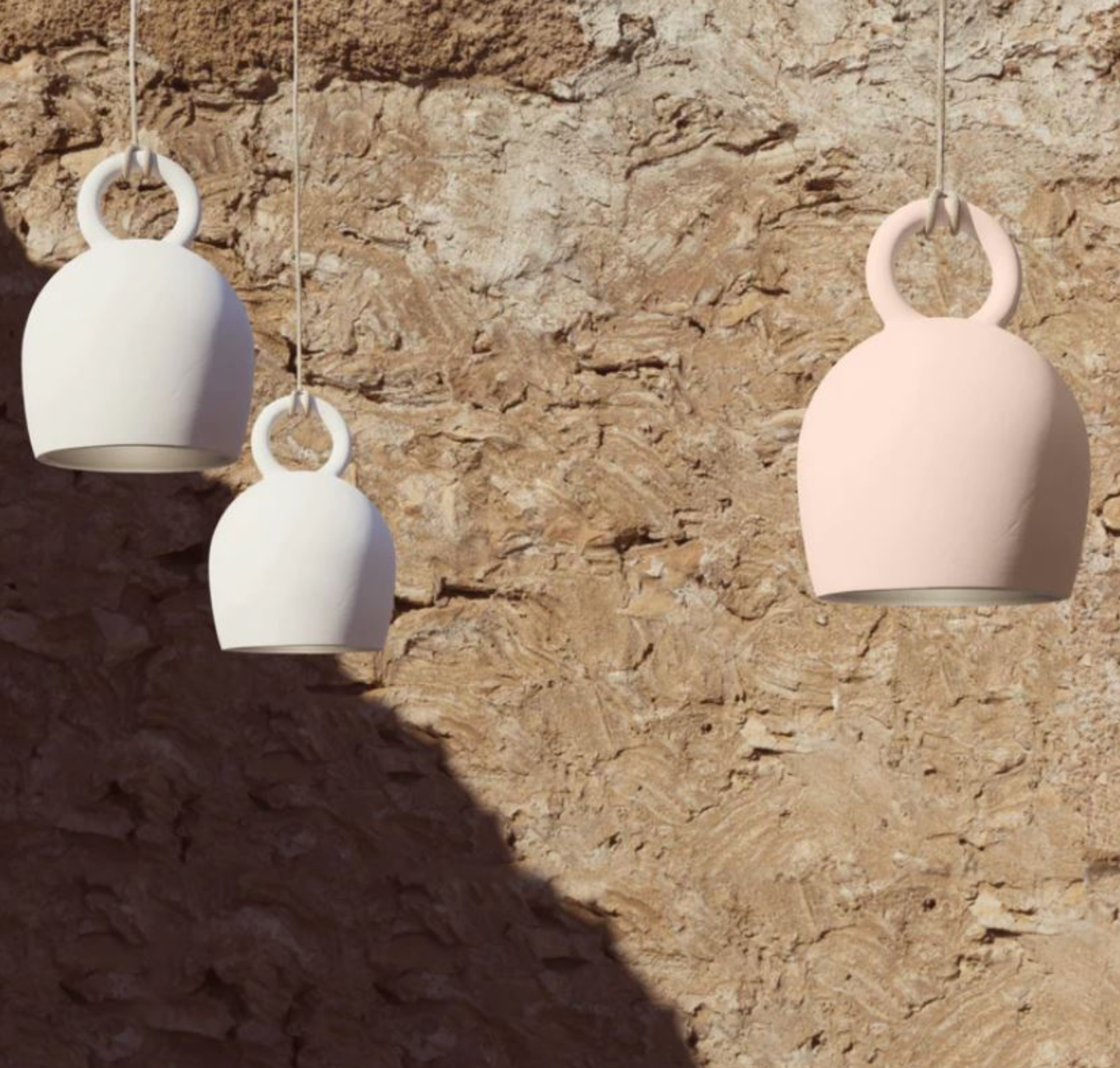 Three hanging ceramic clay pendant lights in white and pink against a stone wall.