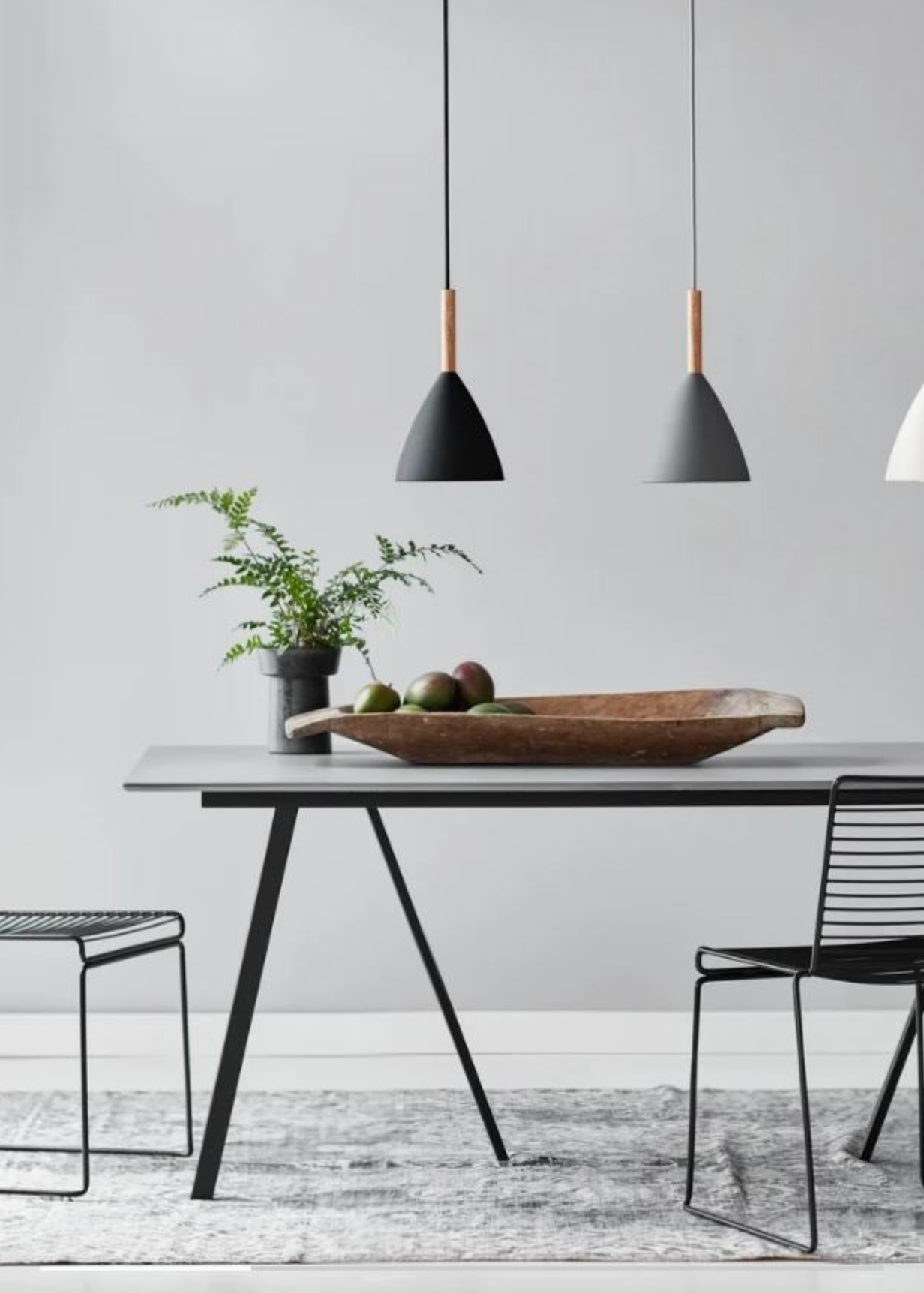 Modern dining area with a table, chairs, and pendant lights against a grey wall.