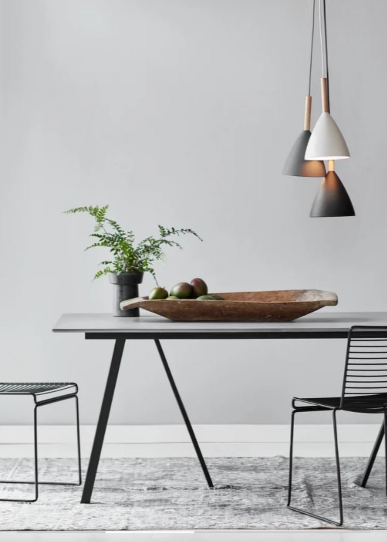 Modern dining area with a table, chairs, and pendant lights against a grey wall.