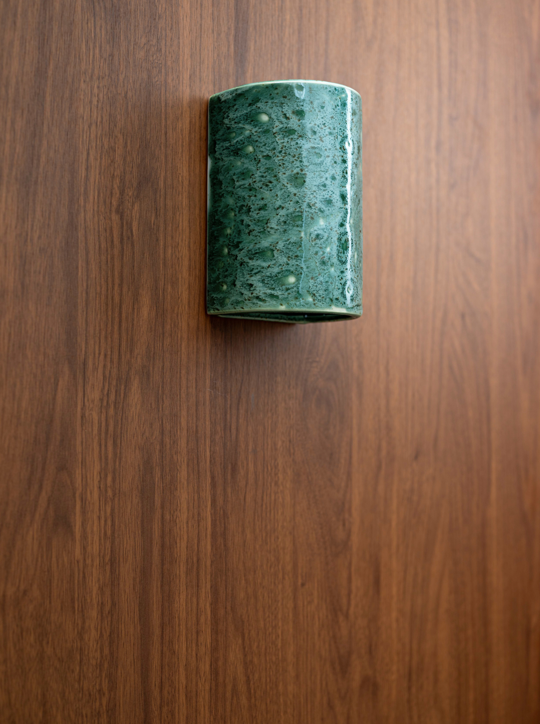 Green cylindrical outdoor clay wall light on a wooden surface