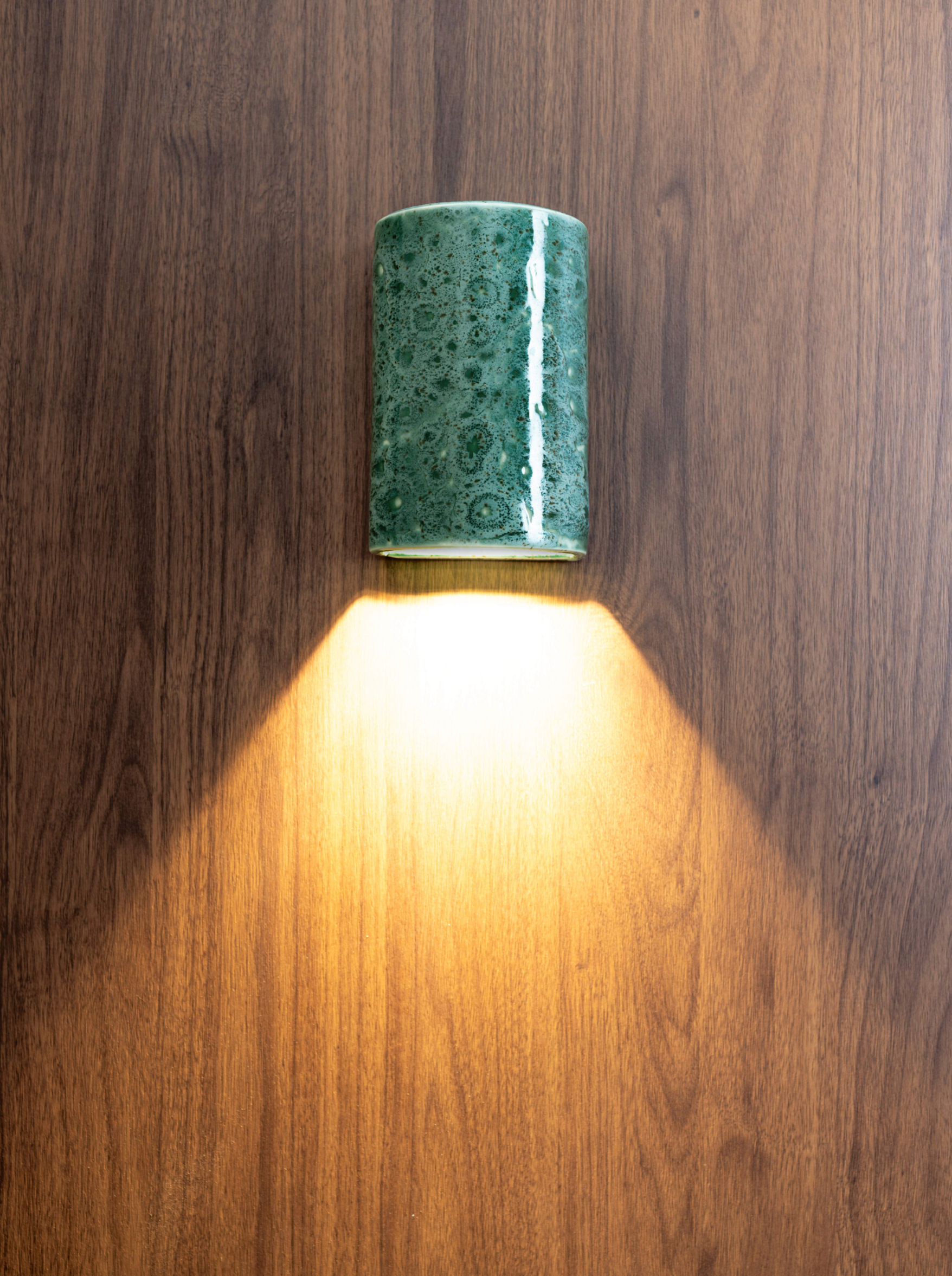 Green ceramic glazed outdoor wall light fixture on a wooden wall