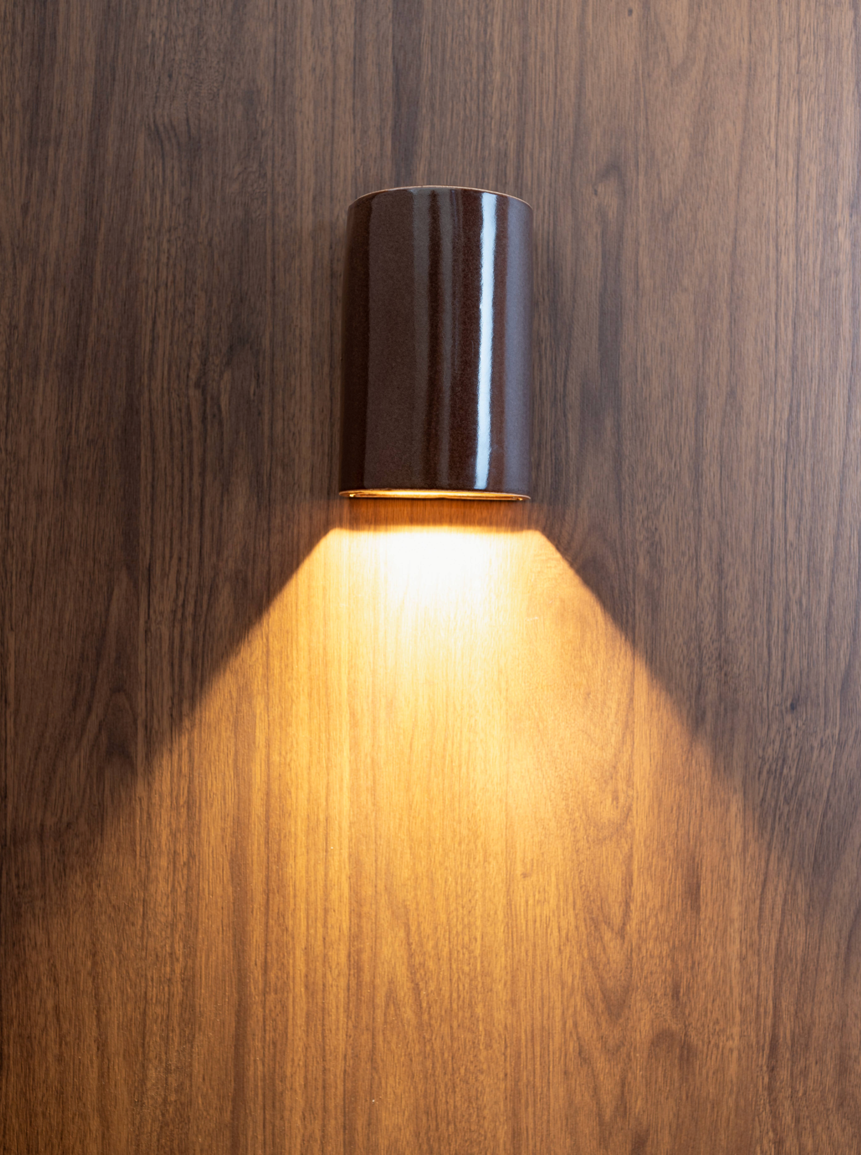 Wall-mounted glazed ceramic outdoor light fixture casting a warm glow on a wooden wall