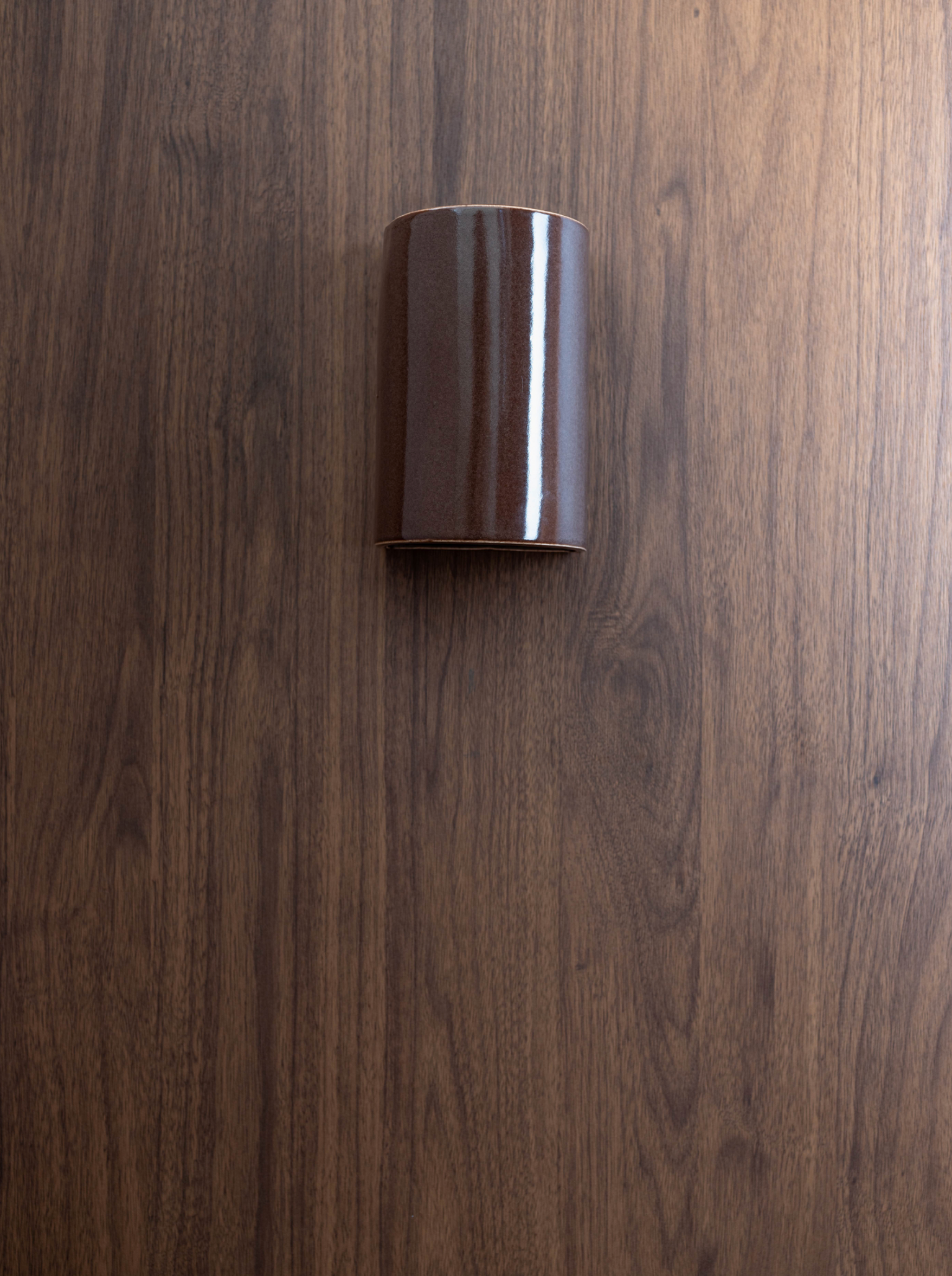 Glazed ceramic cylindrical outdoor wall light on a wooden surface