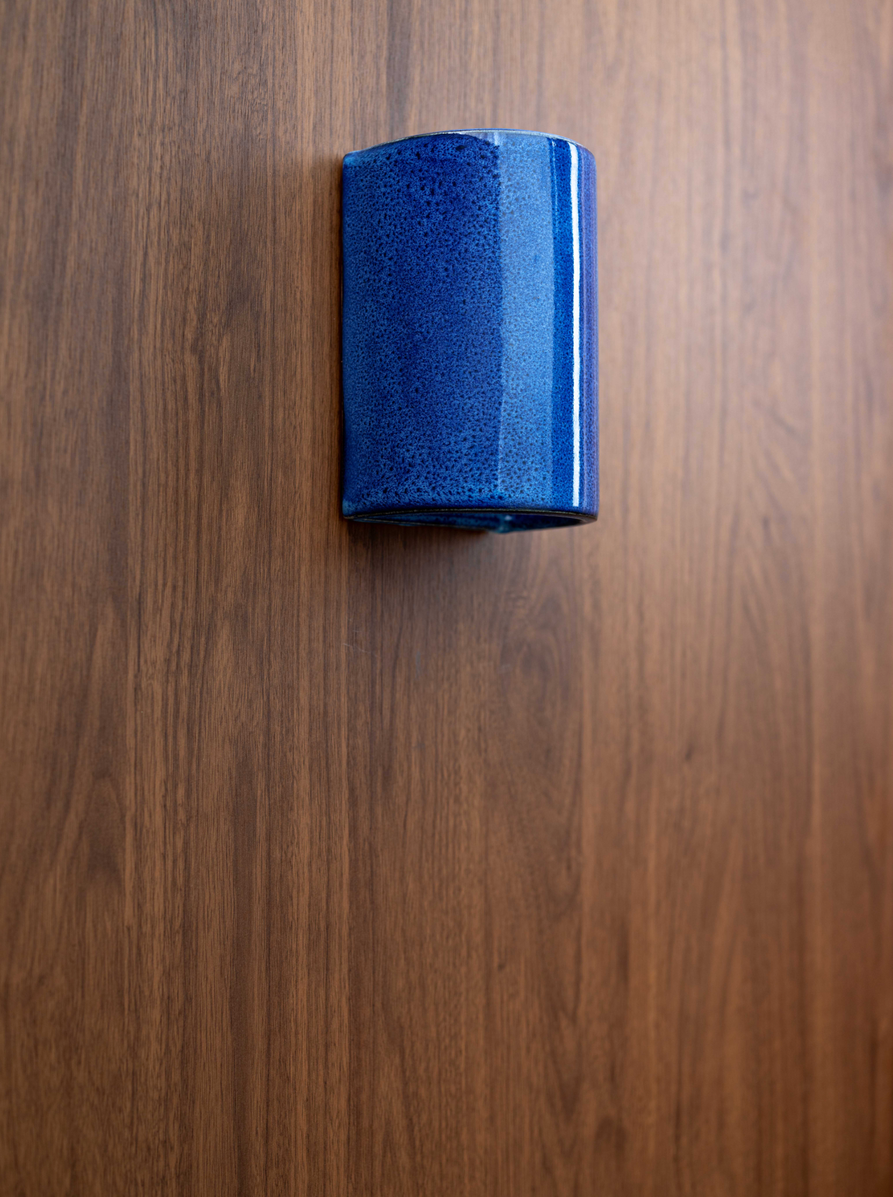 Blue cylindrical glazed ceramic outdoor wall light on a wooden surface