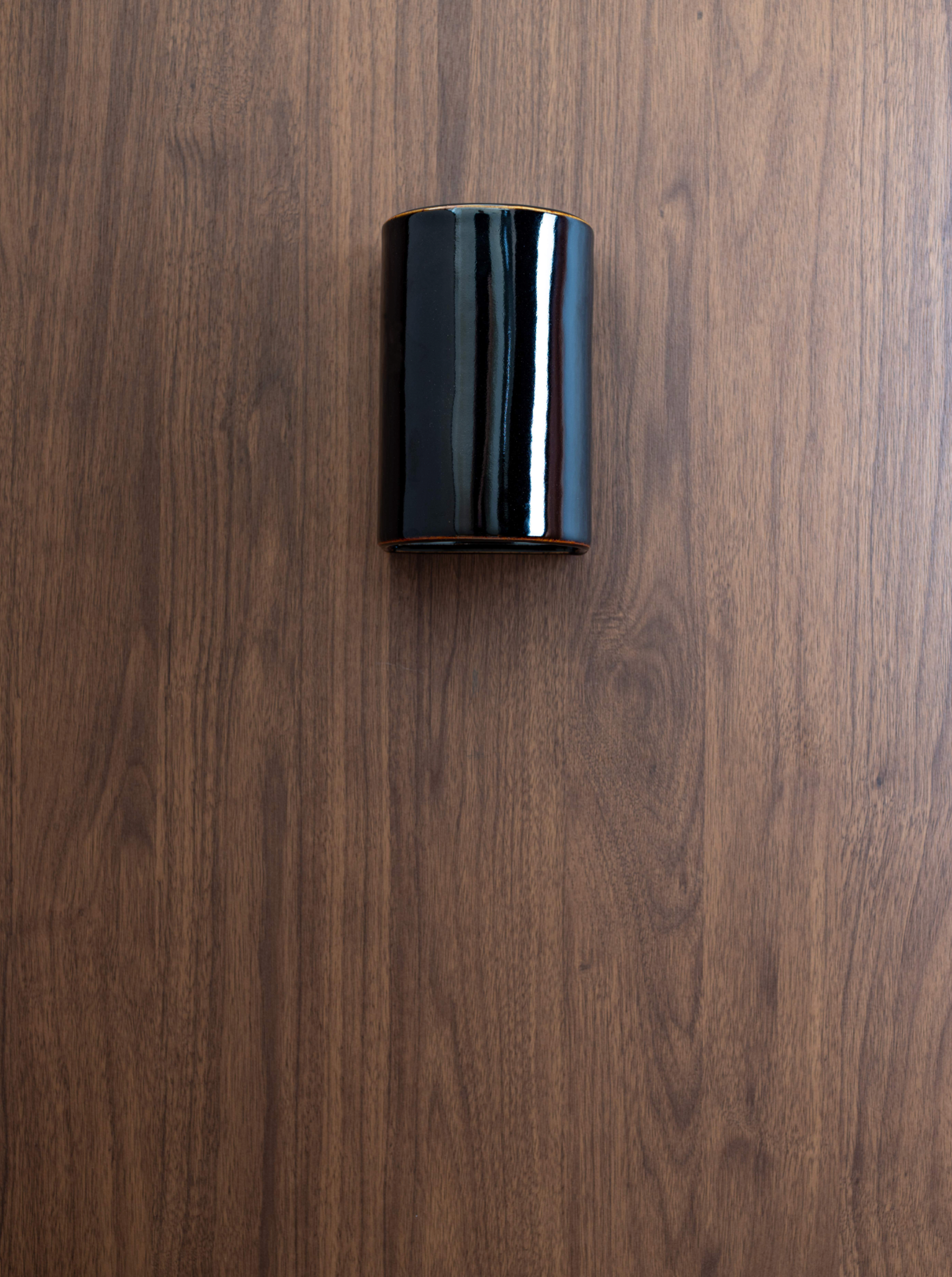Black cylindrical outdoor wall light on a wooden surface
