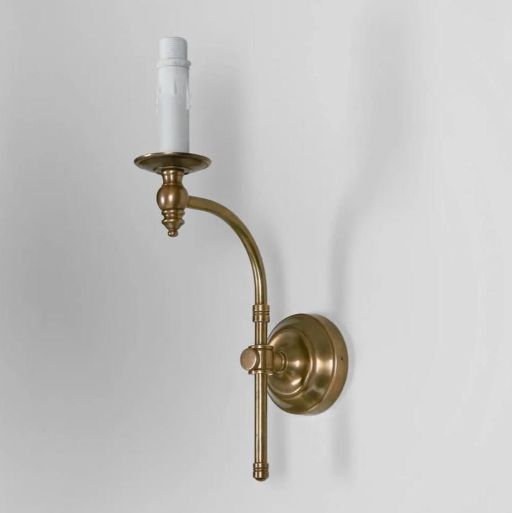 Brass wall sconce with a white candle on a light gray background