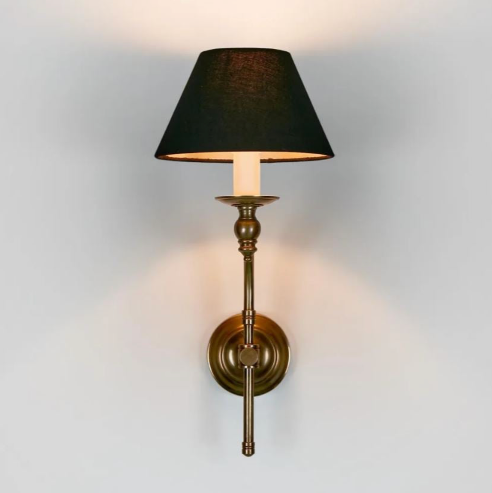 Wall-mounted lamp with black shade and brass base on a light gray background