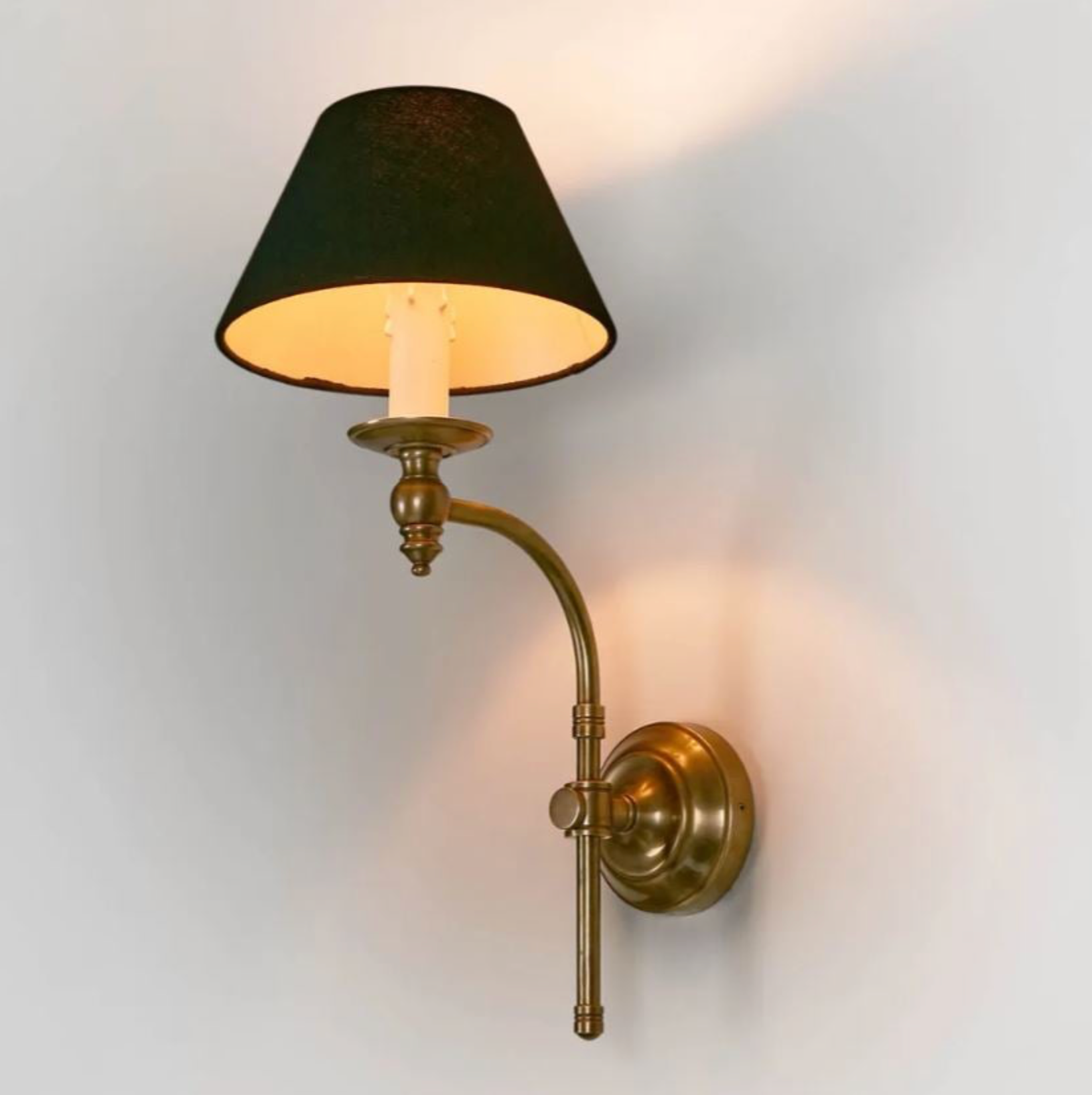 Wall-mounted lamp with black shade and brass arm on a light gray background