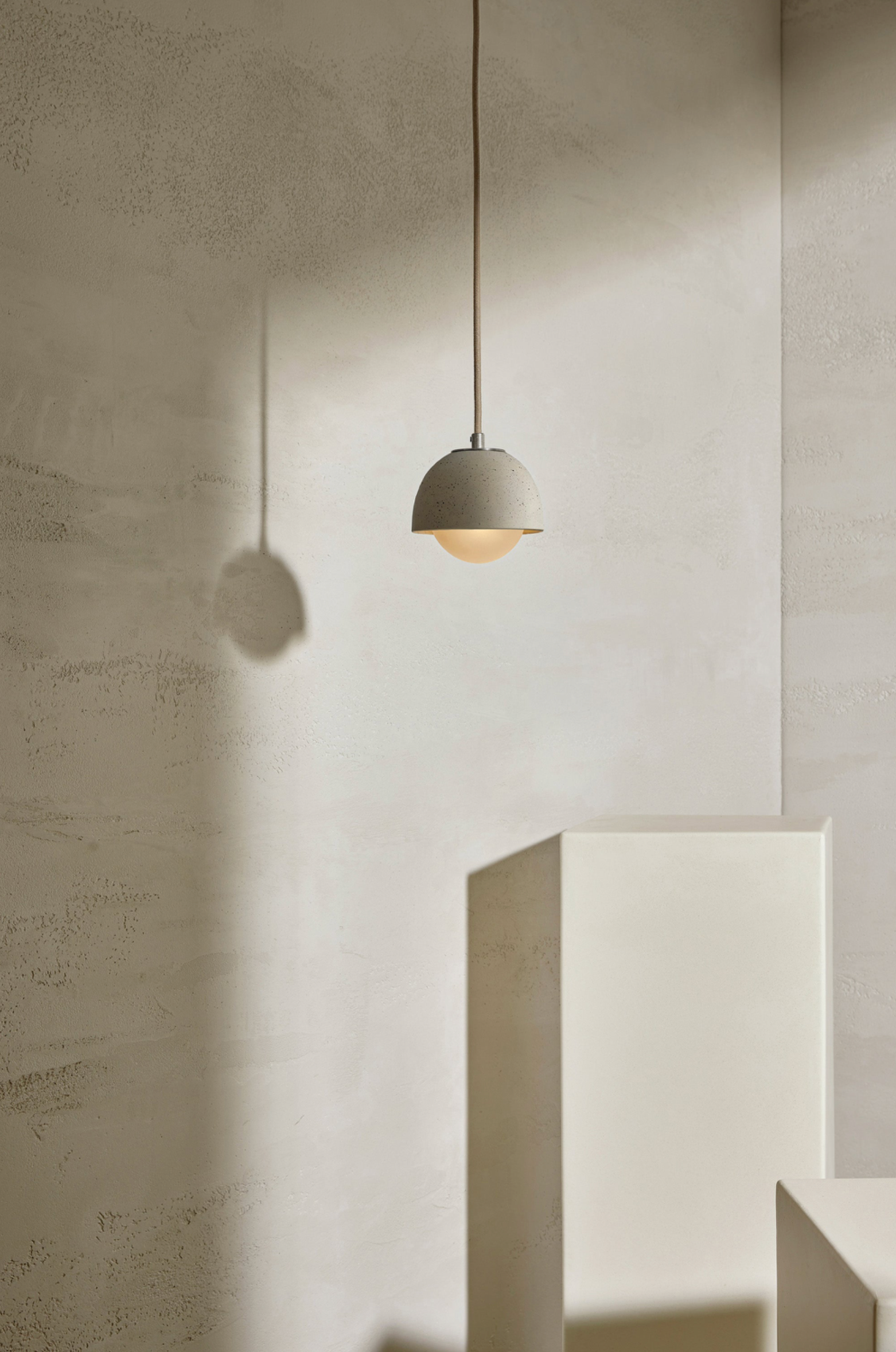 Minimalist ceramic pendant light hanging against a neutral wall.