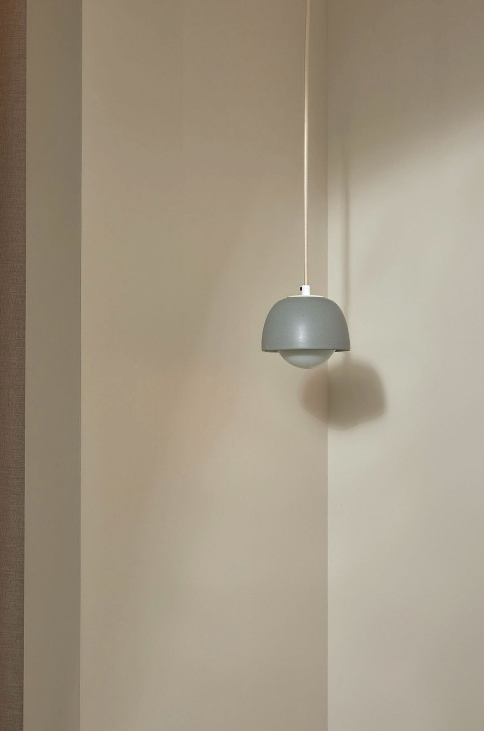 Grey pendant light hanging against a beige wall