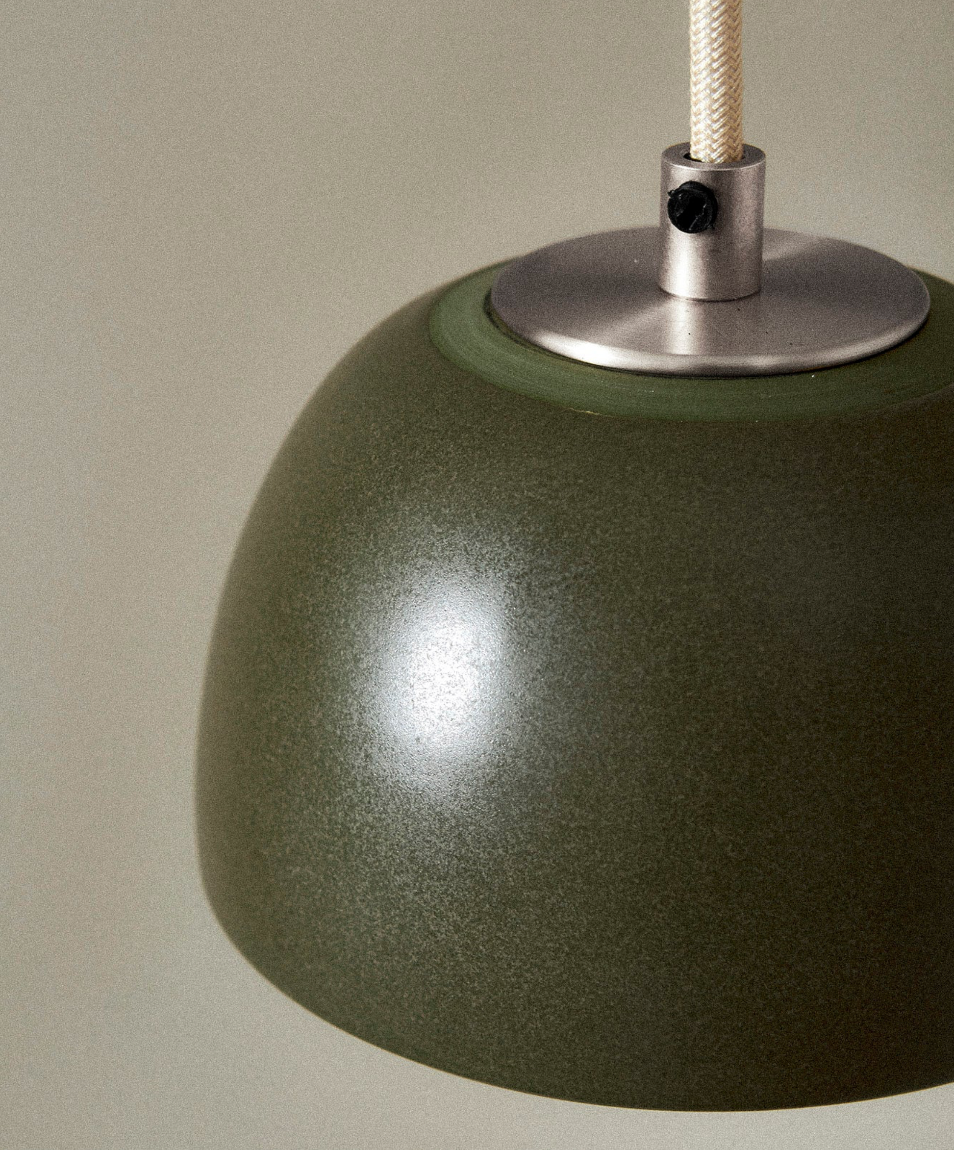 Close-up of a green pendant lamp with a metallic fitting on a neutral background