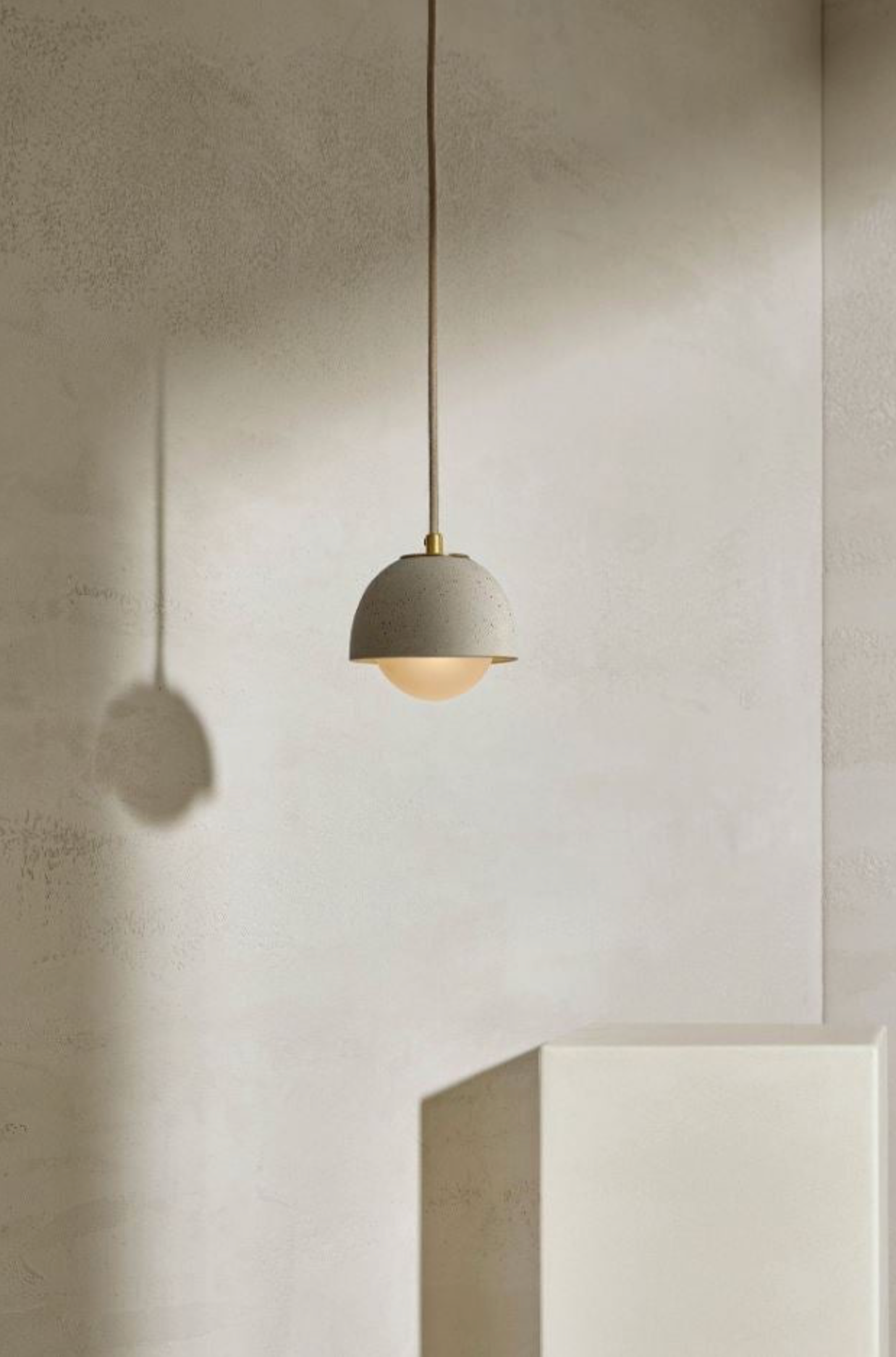 Minimalist pendant light hanging against a plain wall with a concrete block in the foreground.
