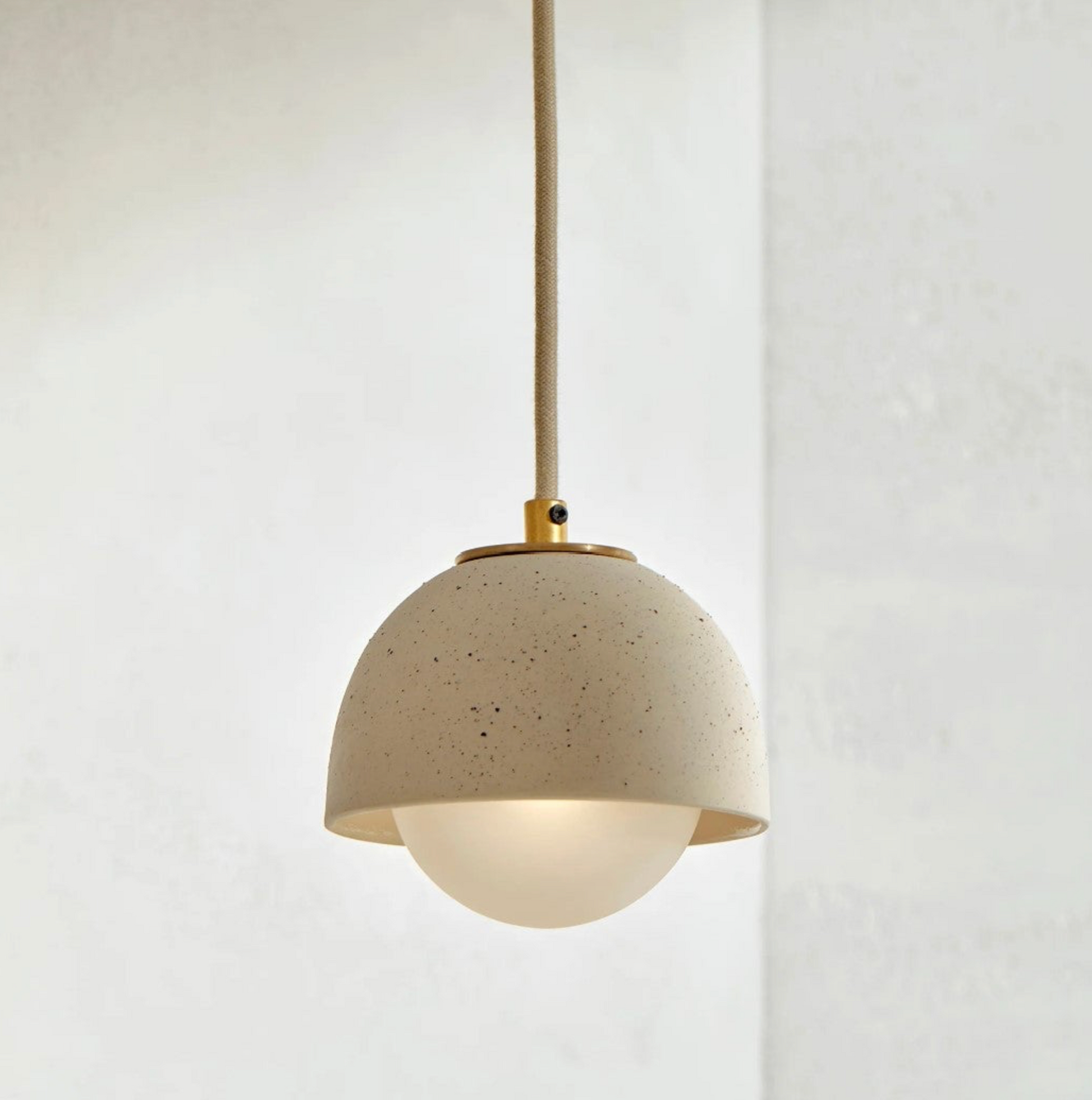 Pendant light with beige terrazzo shade and brass accents on a white background