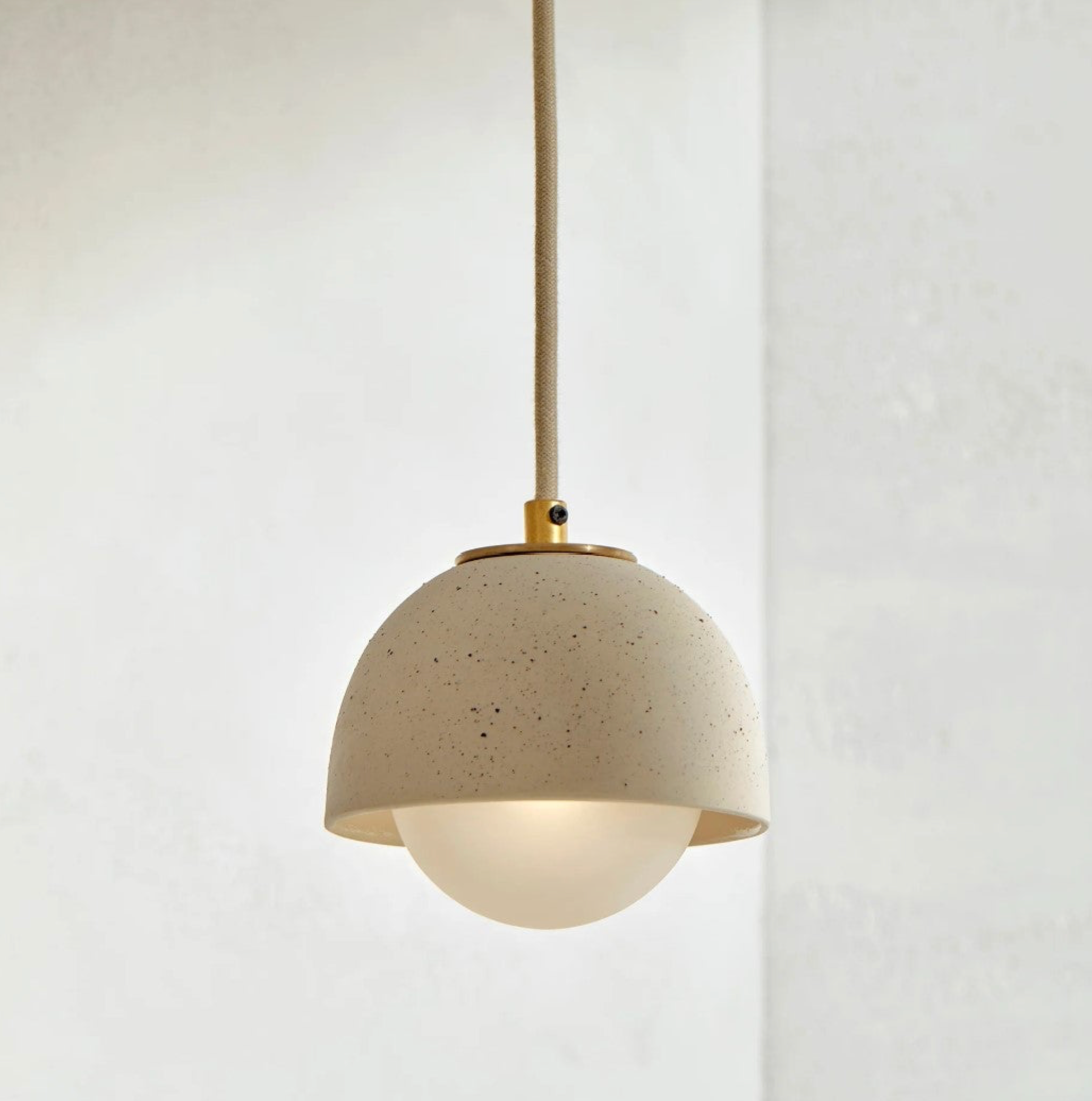 Pendant light with beige terrazzo shade and brass accents on a white background