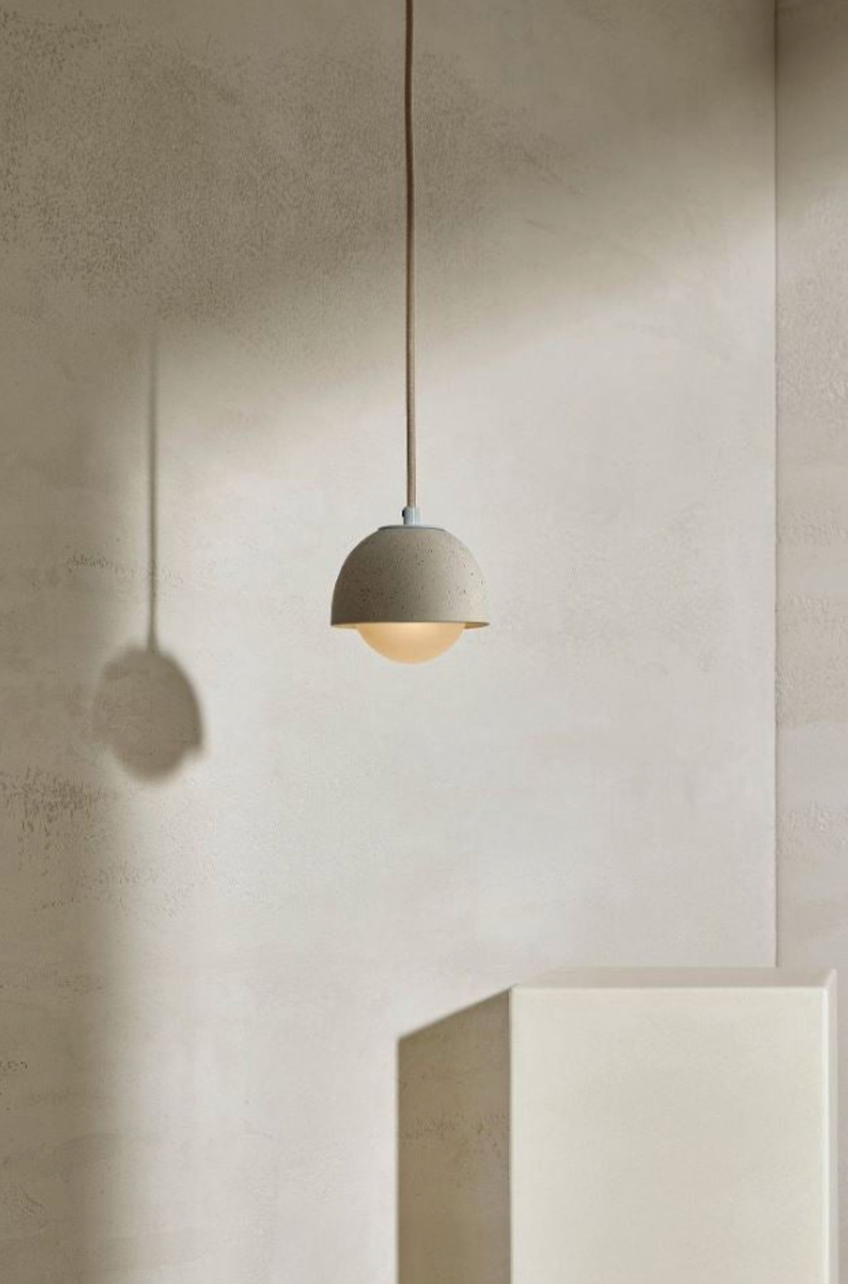Minimalist pendant light hanging against a plain wall with a neutral color palette.