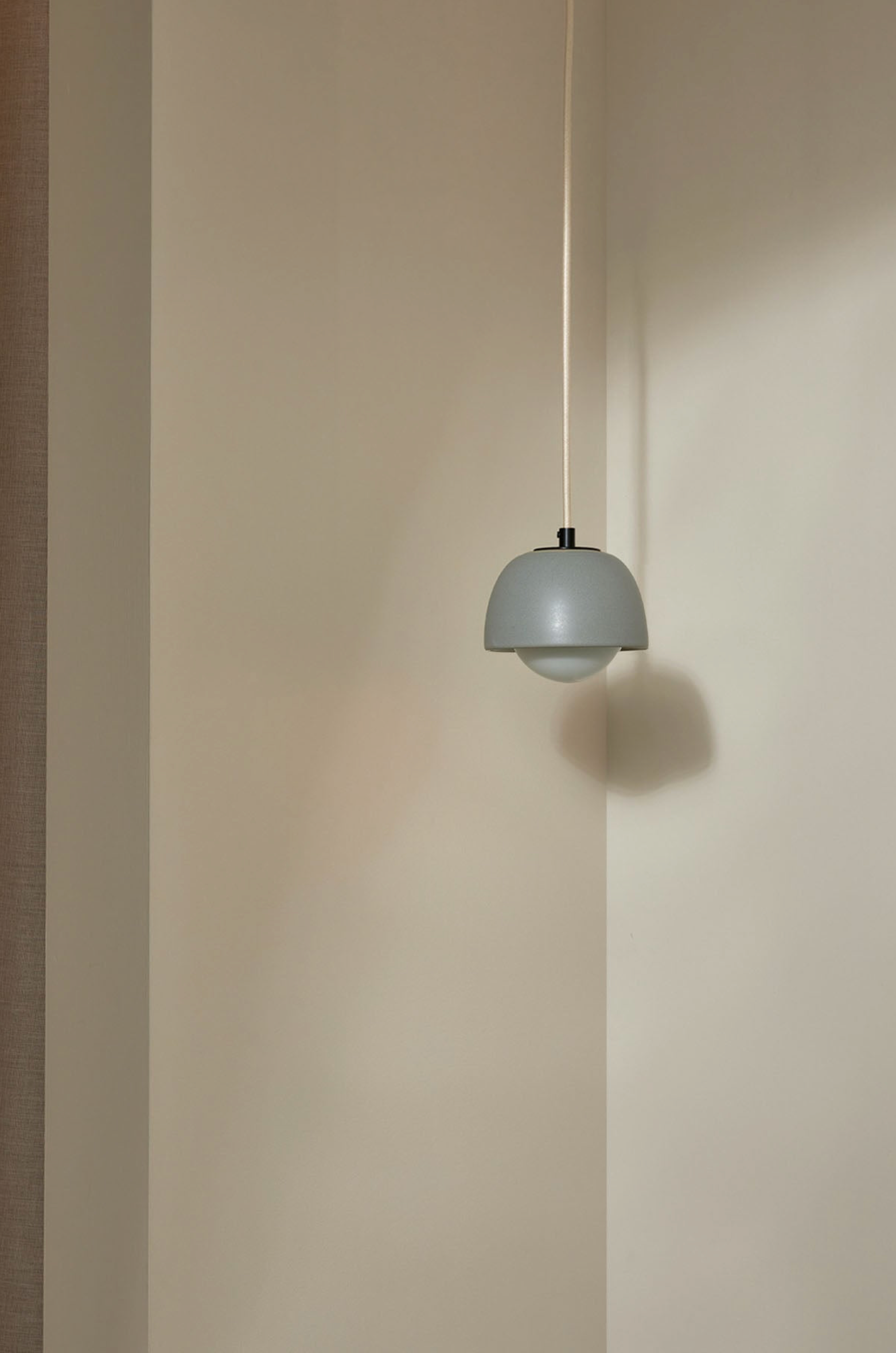 Grey pendant light hanging against a beige wall