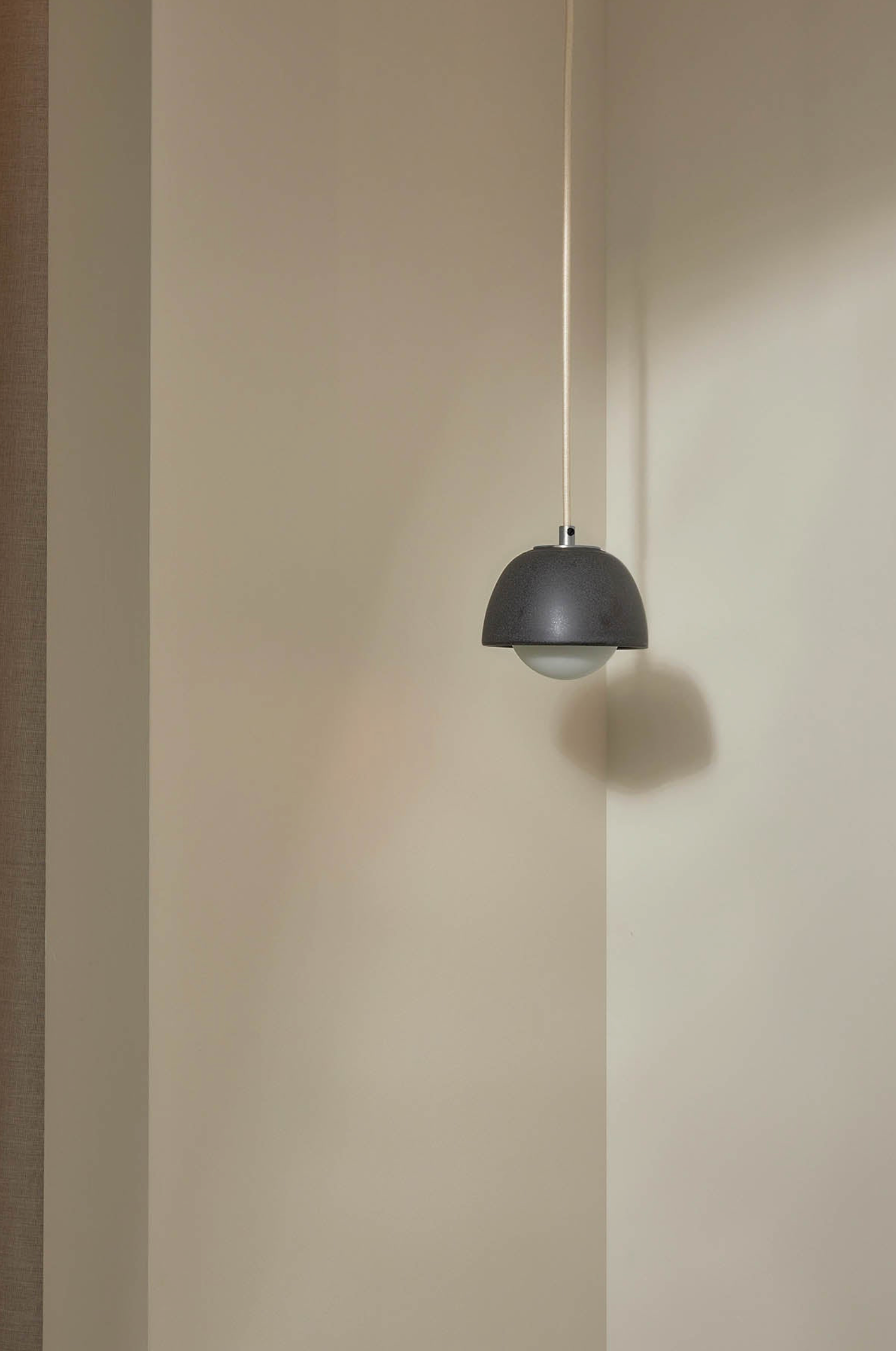 Black ceramic pendant light hanging against a beige wall