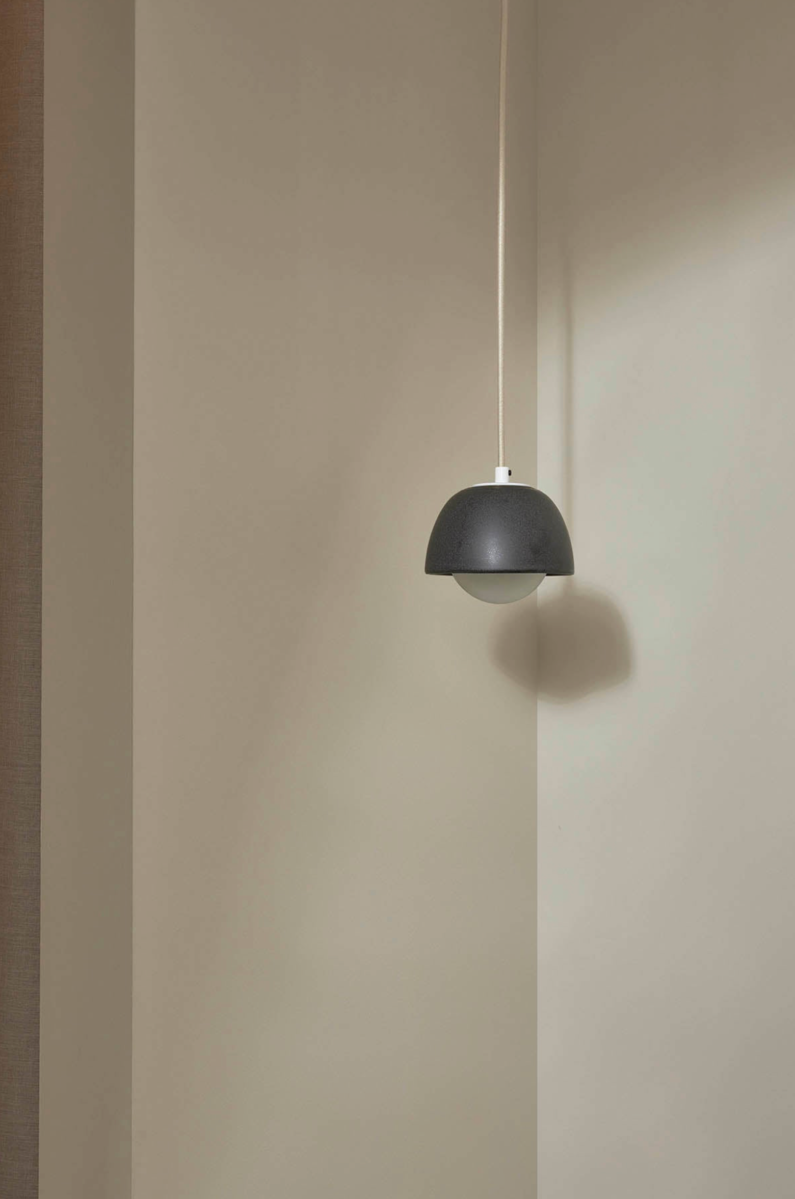 Black ceramic pendant light hanging against a beige wall