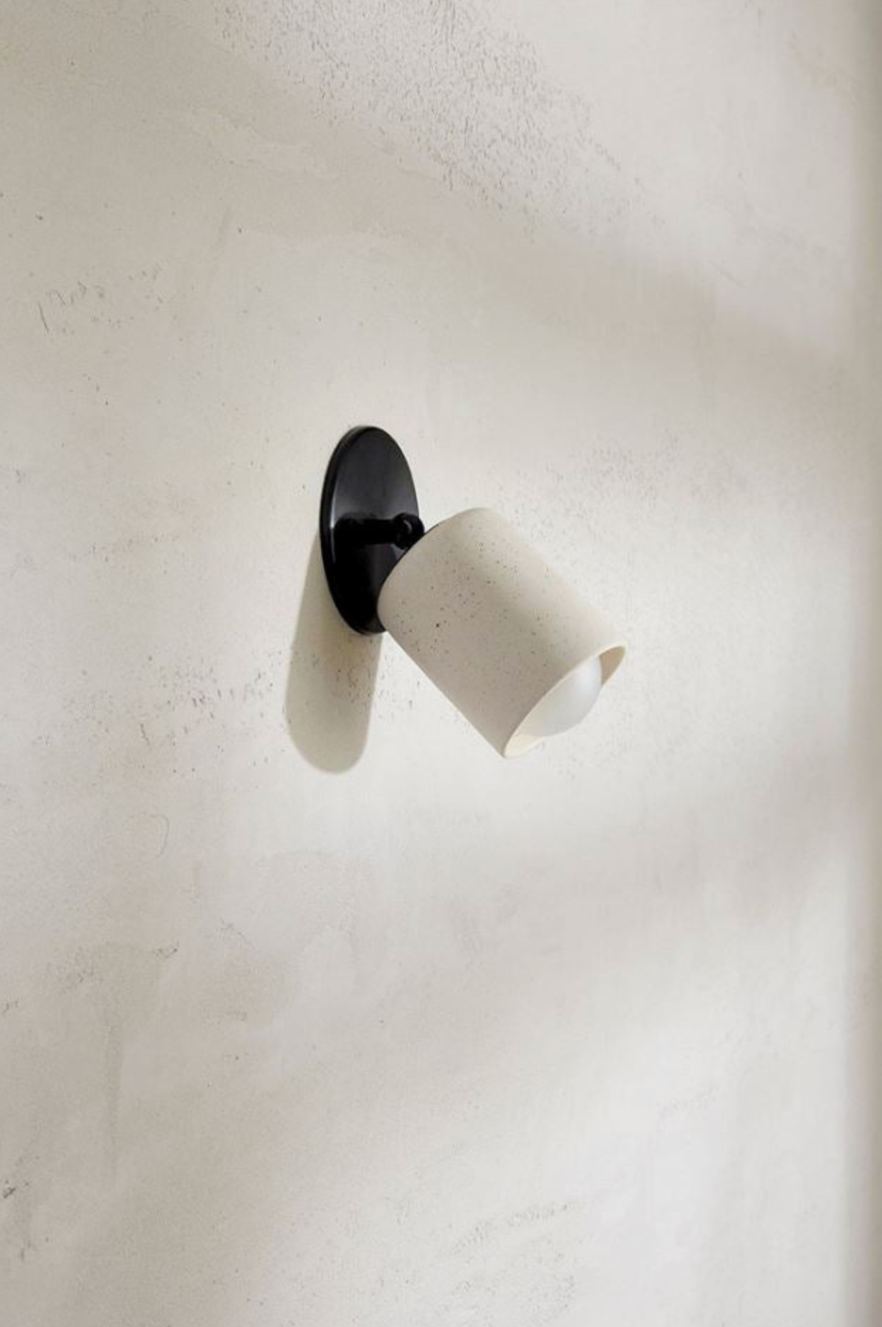 Wall-mounted light fixture with white shade and black base on a plain wall.