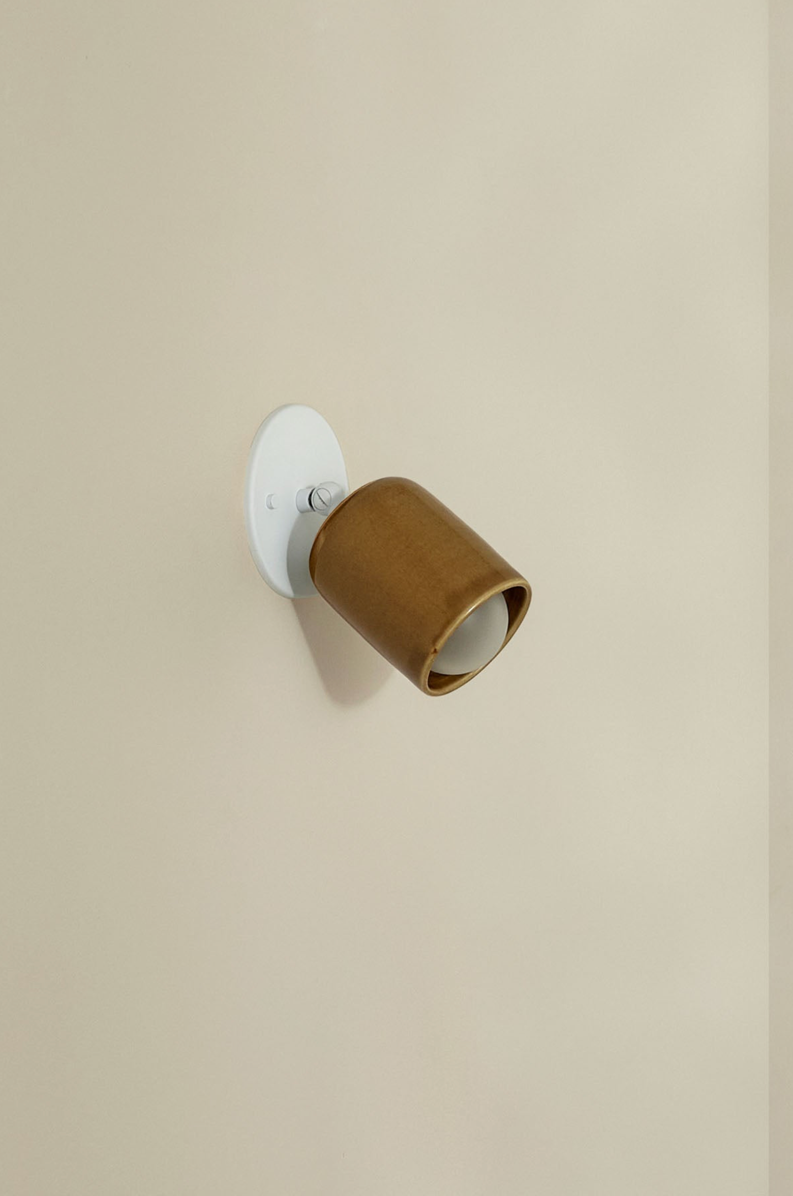 Small wall-mounted light fixture with a brown shade on a beige wall.