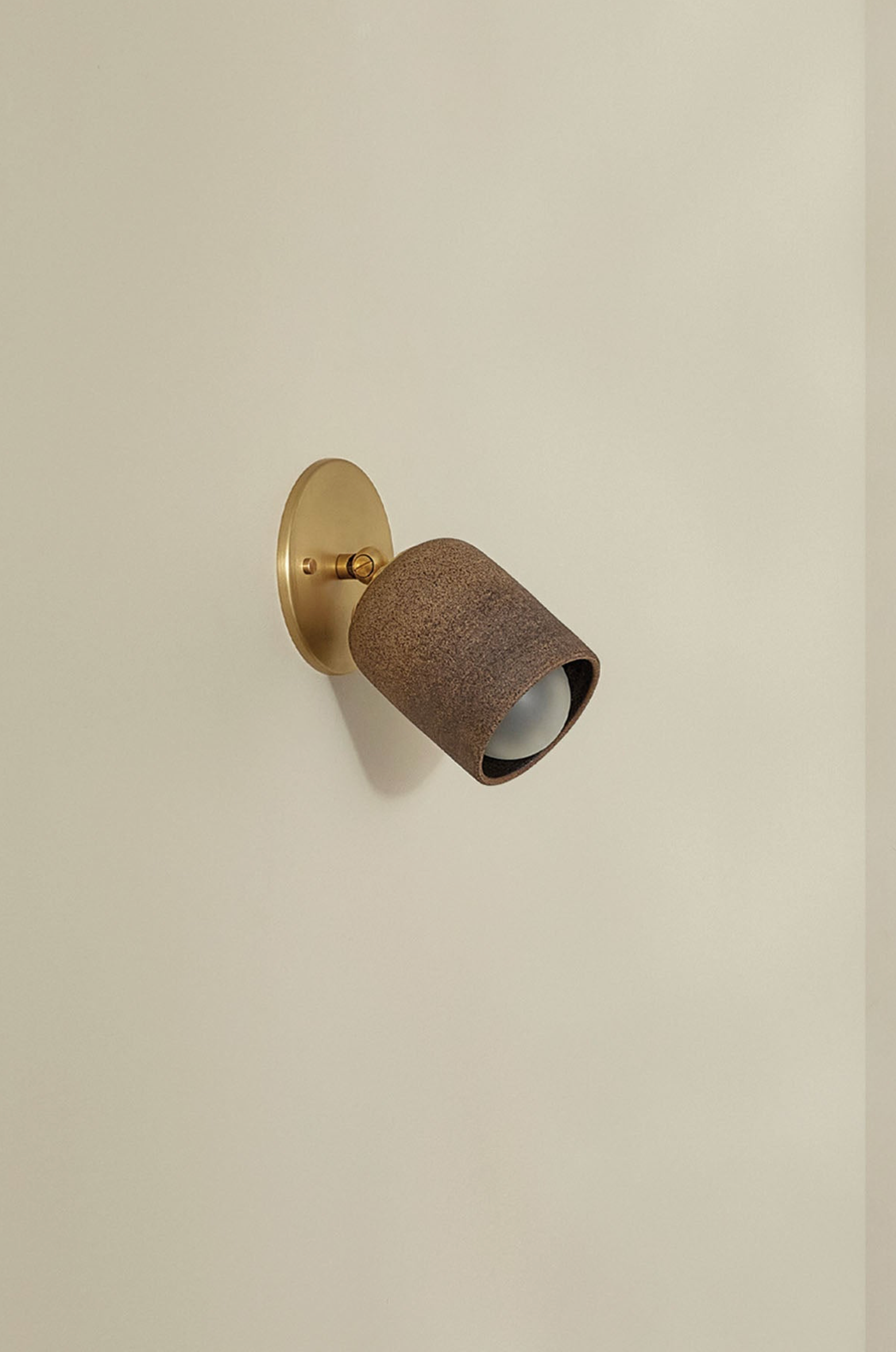 Wall-mounted light fixture with brown textured shade on a beige wall