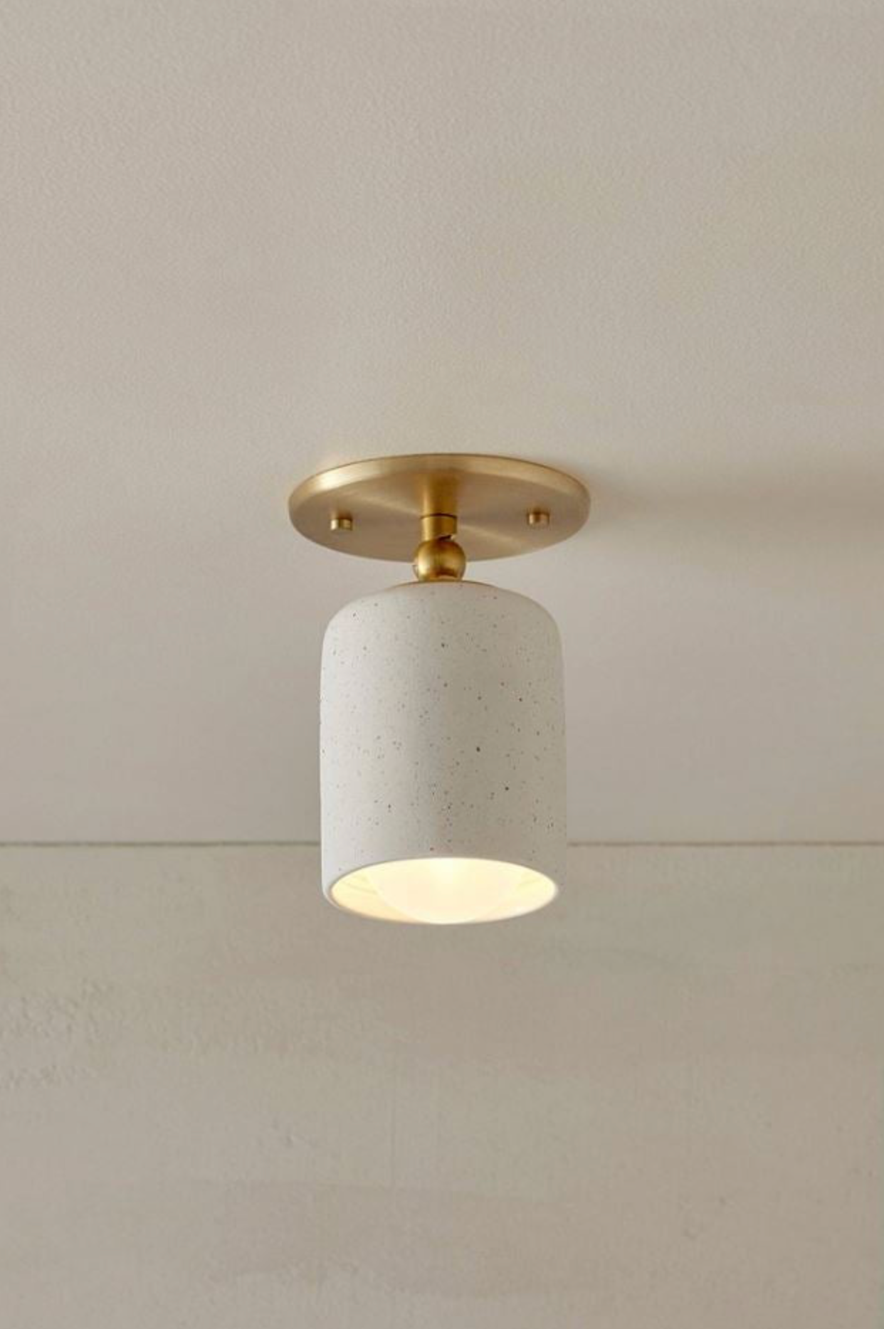 Ceiling light fixture with ceramic base and gold fixture on a neutral background