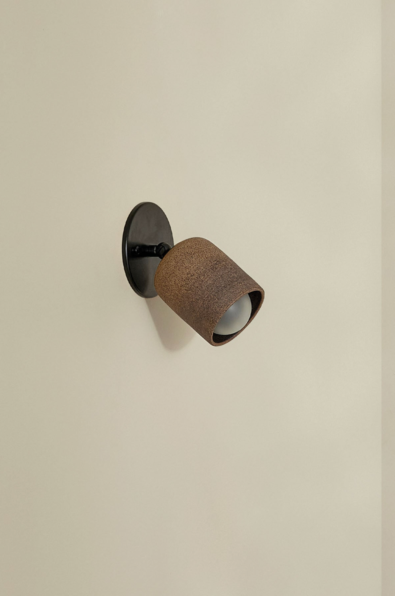 Wall-mounted light fixture with brown textured shade on a beige wall