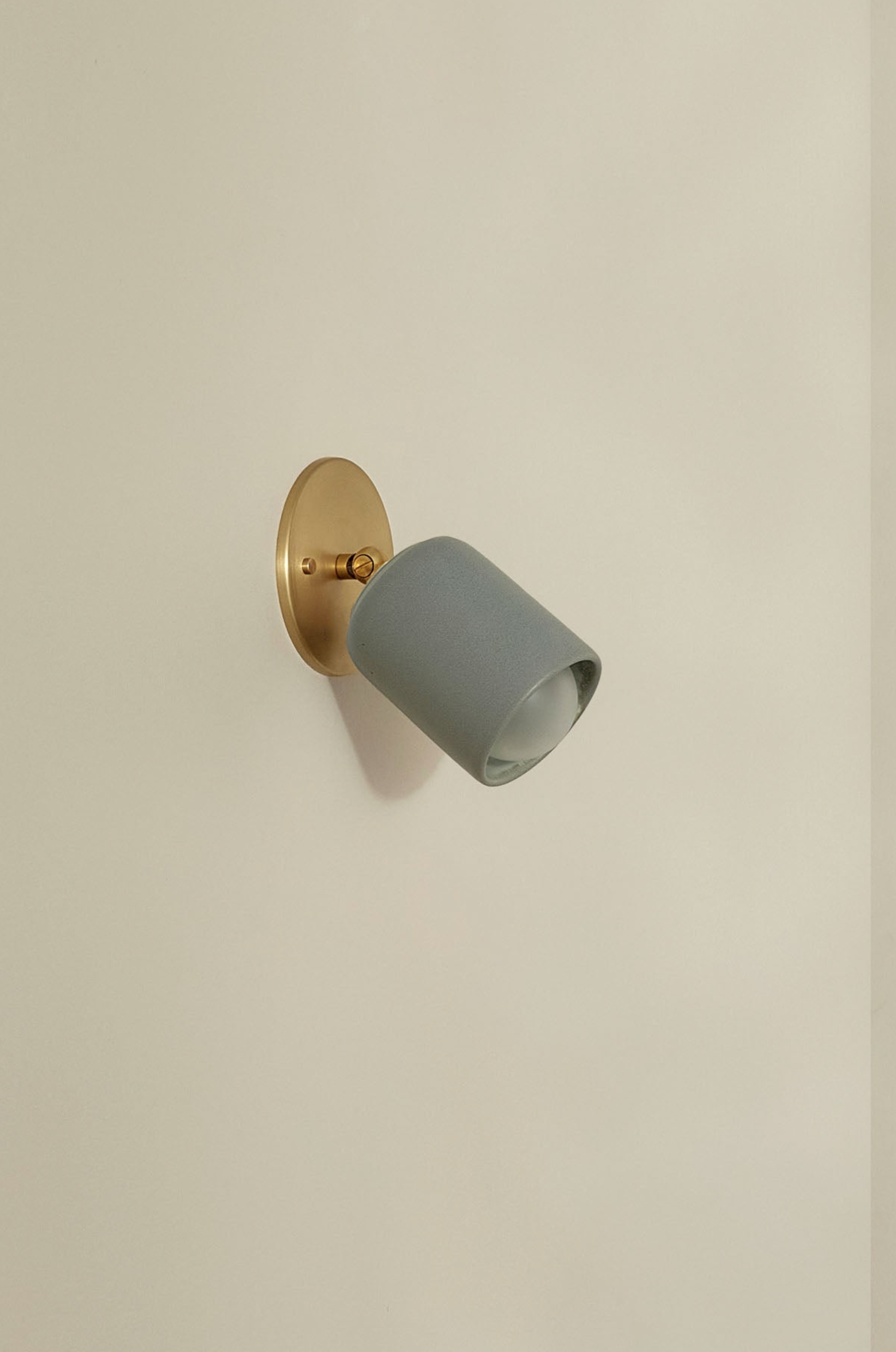 Wall-mounted light fixture with a grey ceramic shade and gold fixture on a beige wall.