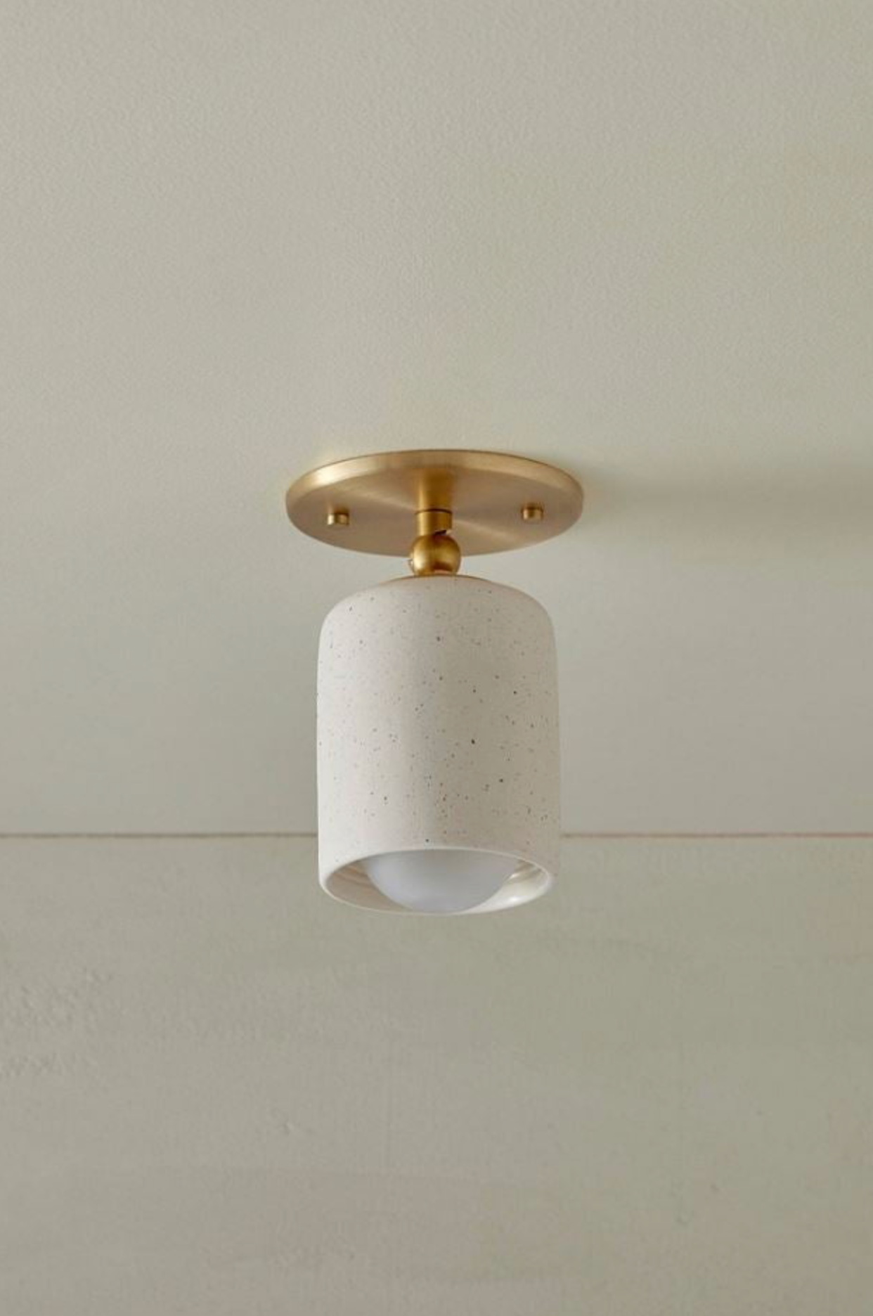Ceiling light fixture with gold fixture and white ceramic shade on a neutral ceiling.