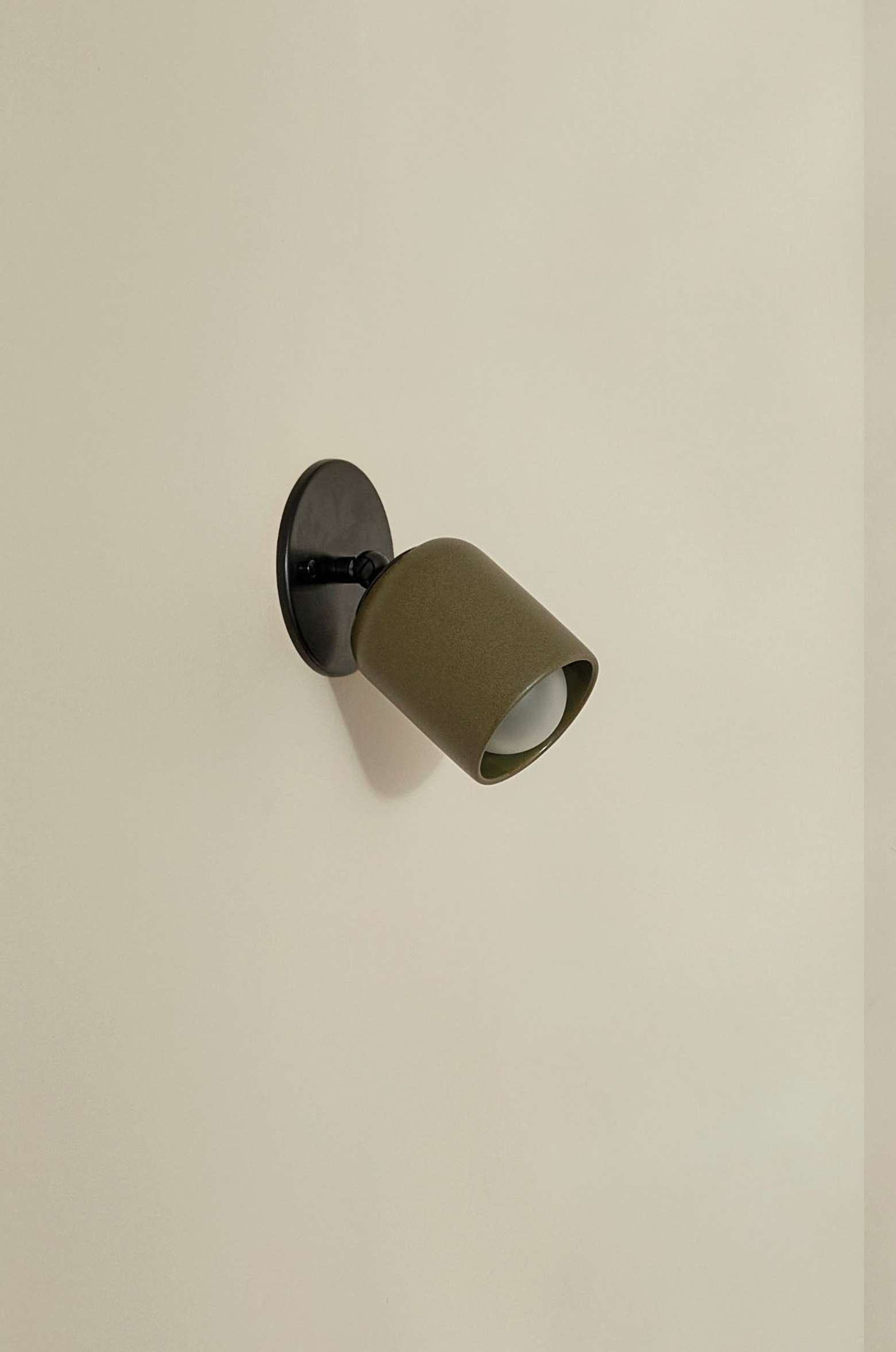 Wall-mounted light fixture with ceramic olive green shade and black base on a beige wall.