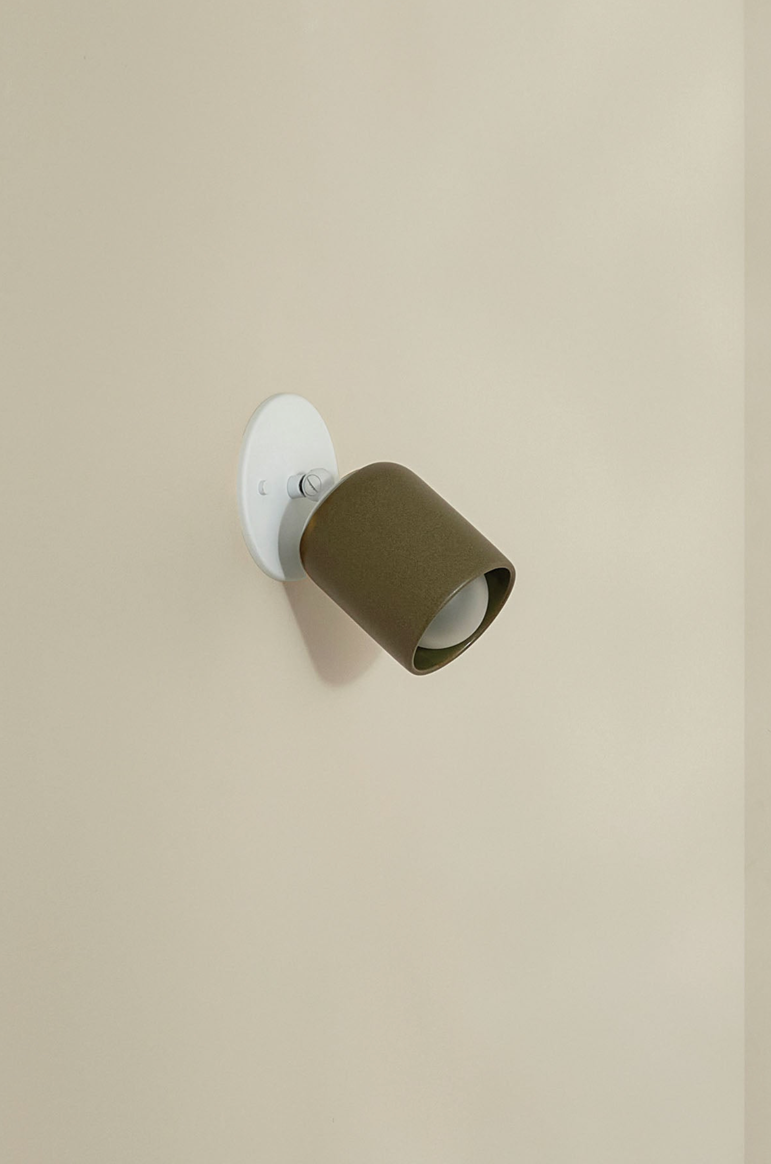 Wall-mounted light fixture with olive green shade on a beige wall