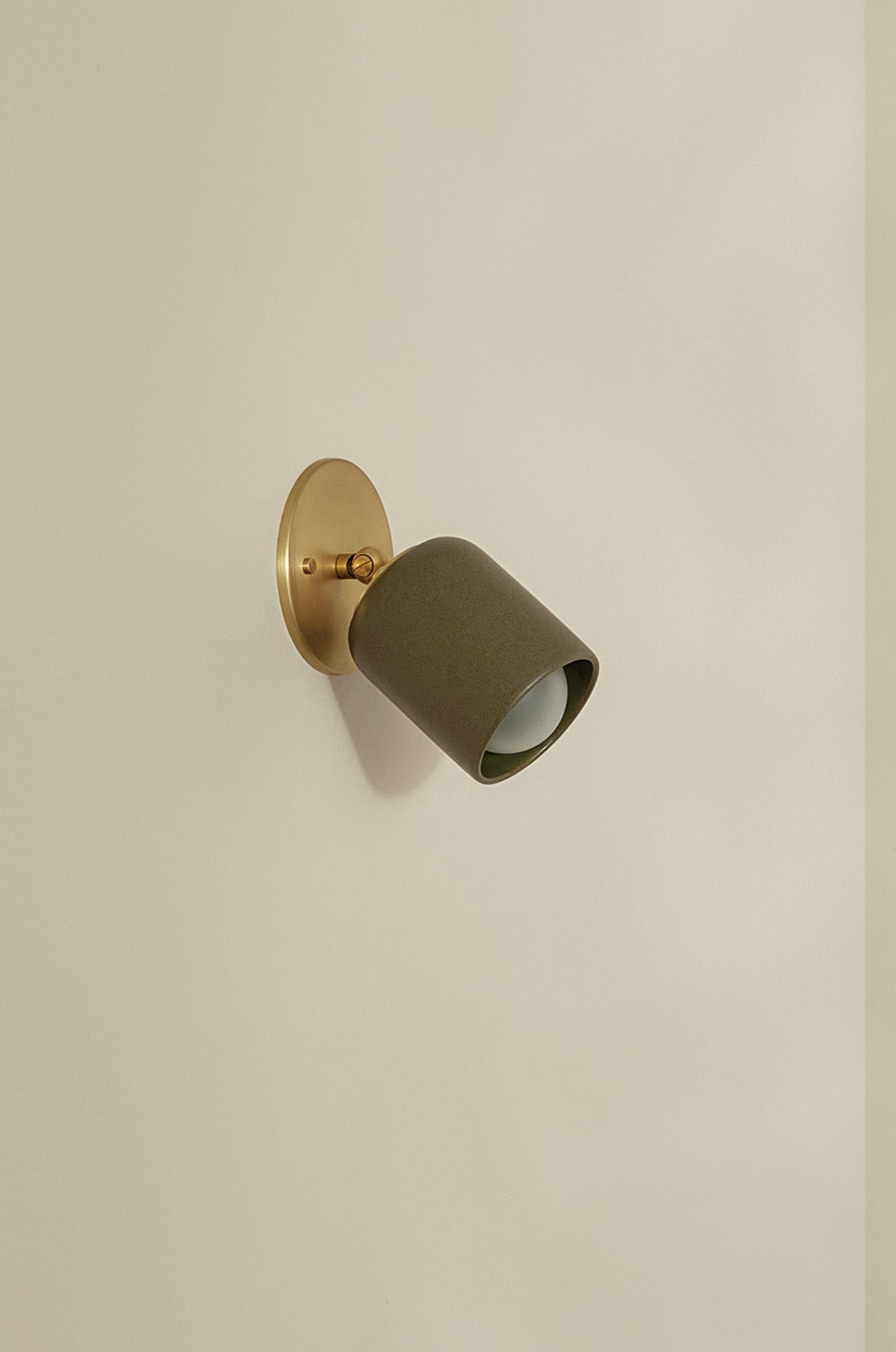 Wall-mounted light fixture with green shade and gold base on a beige wall