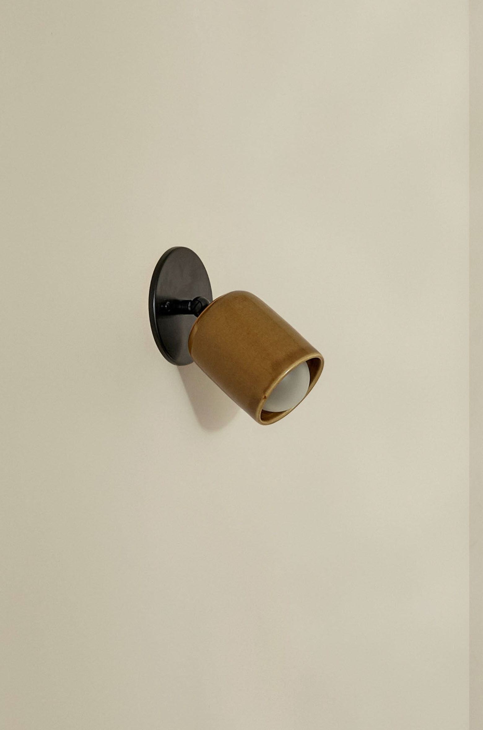 Wall-mounted light fixture with ceramic brown shade on a beige wall