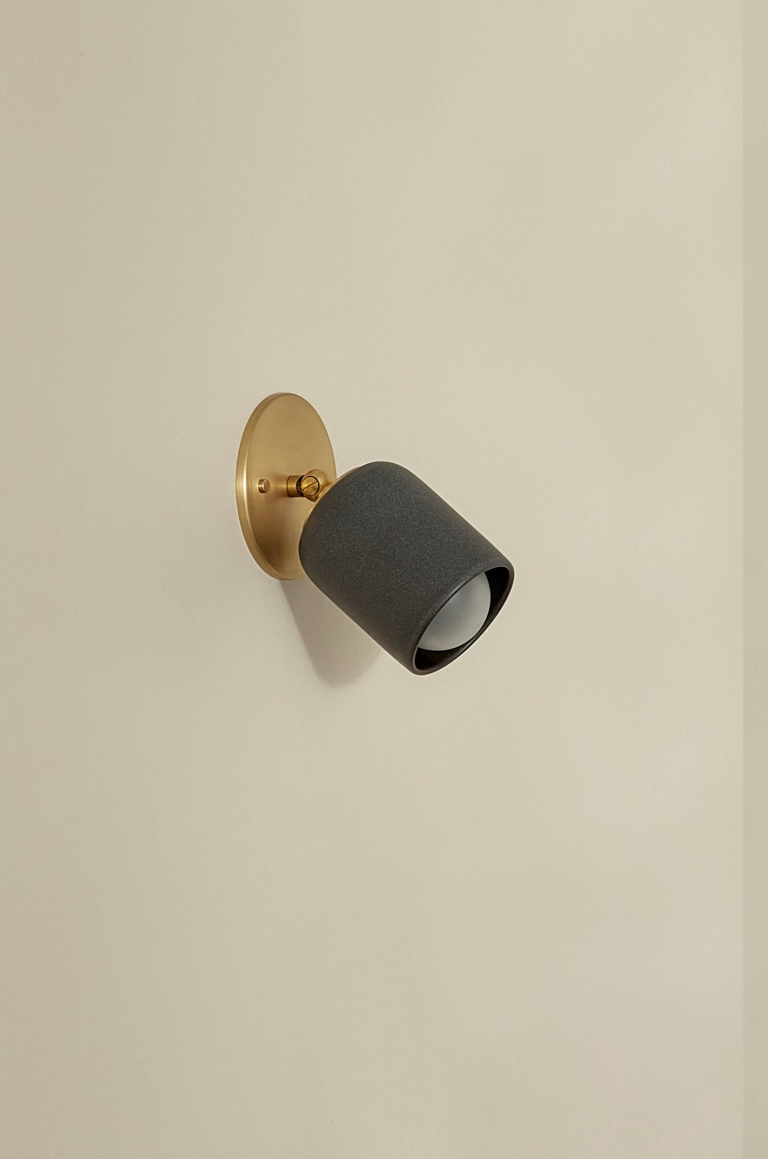 Wall-mounted ceramic light fixture with black shade and gold base on a beige wall
