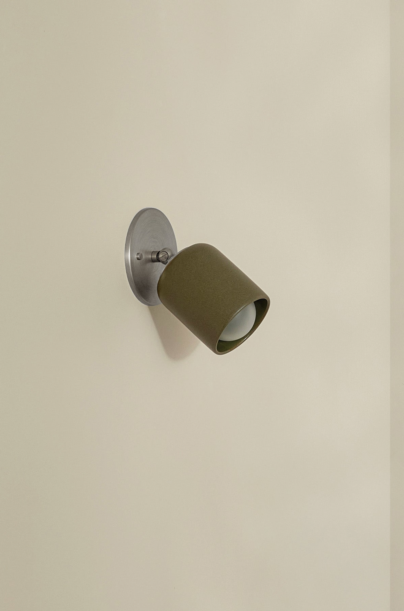 Wall-mounted light fixture with olive green shade on a beige wall